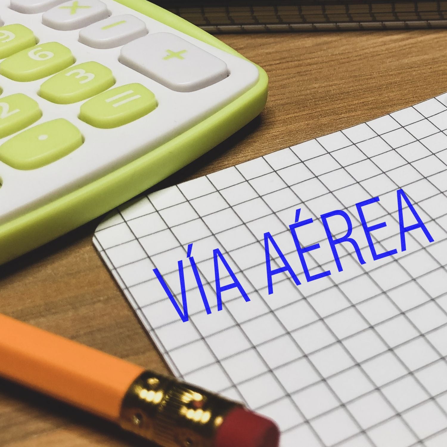 Via Aerea rubber stamp on graph paper next to a pencil and a calculator on a wooden desk.