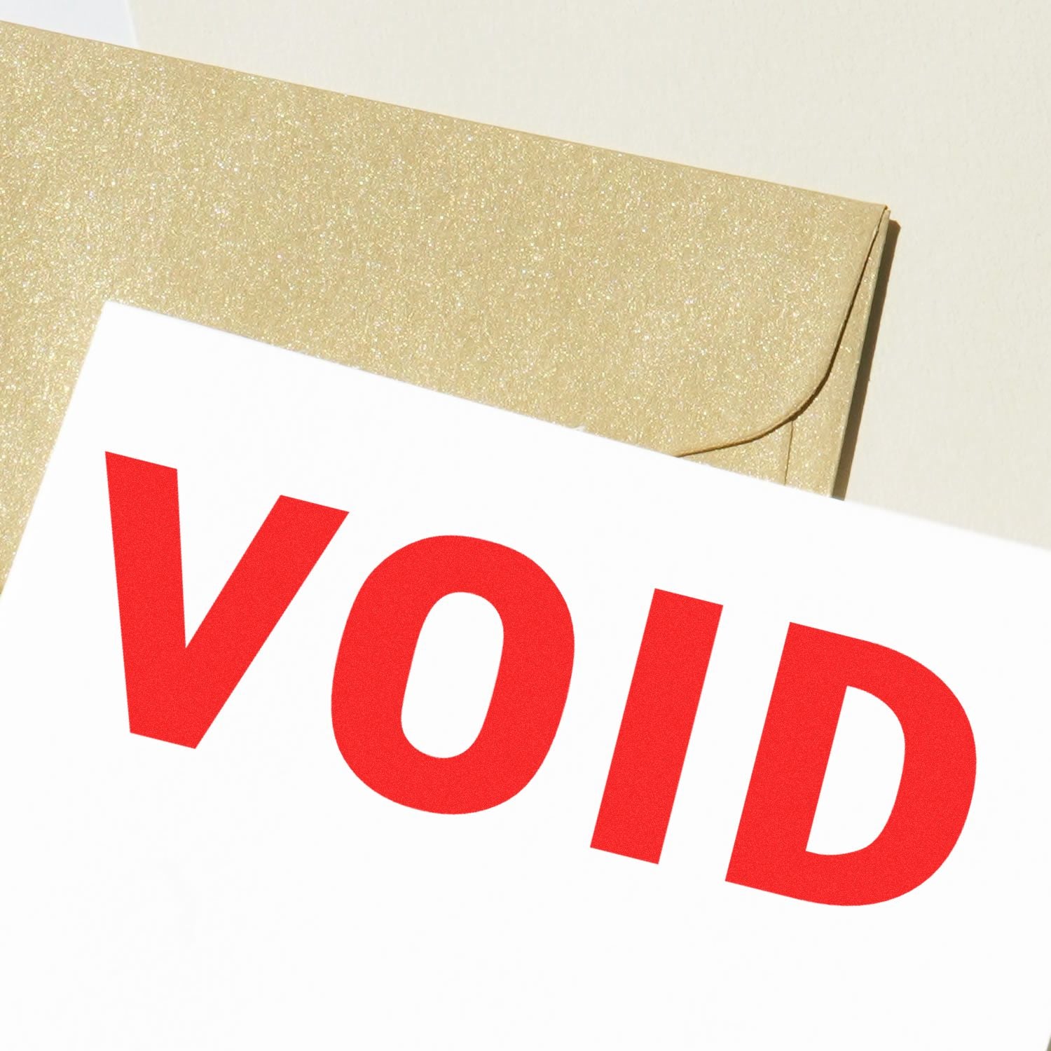 Close-up of a red 'VOID' rubber stamp mark on a white paper, with a gold envelope in the background.