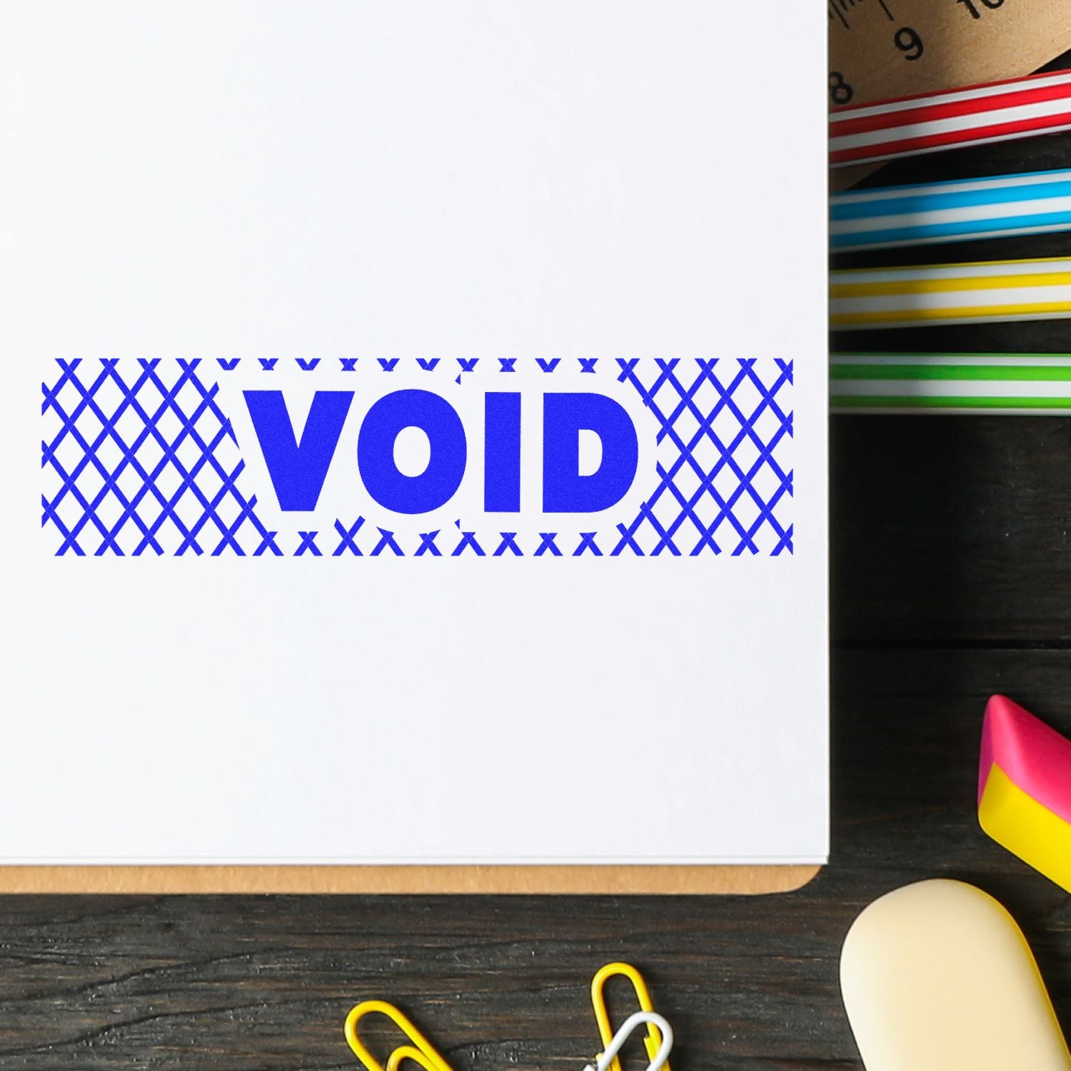 Void with Strikelines Rubber Stamp in blue ink on white paper, surrounded by office supplies on a wooden desk.