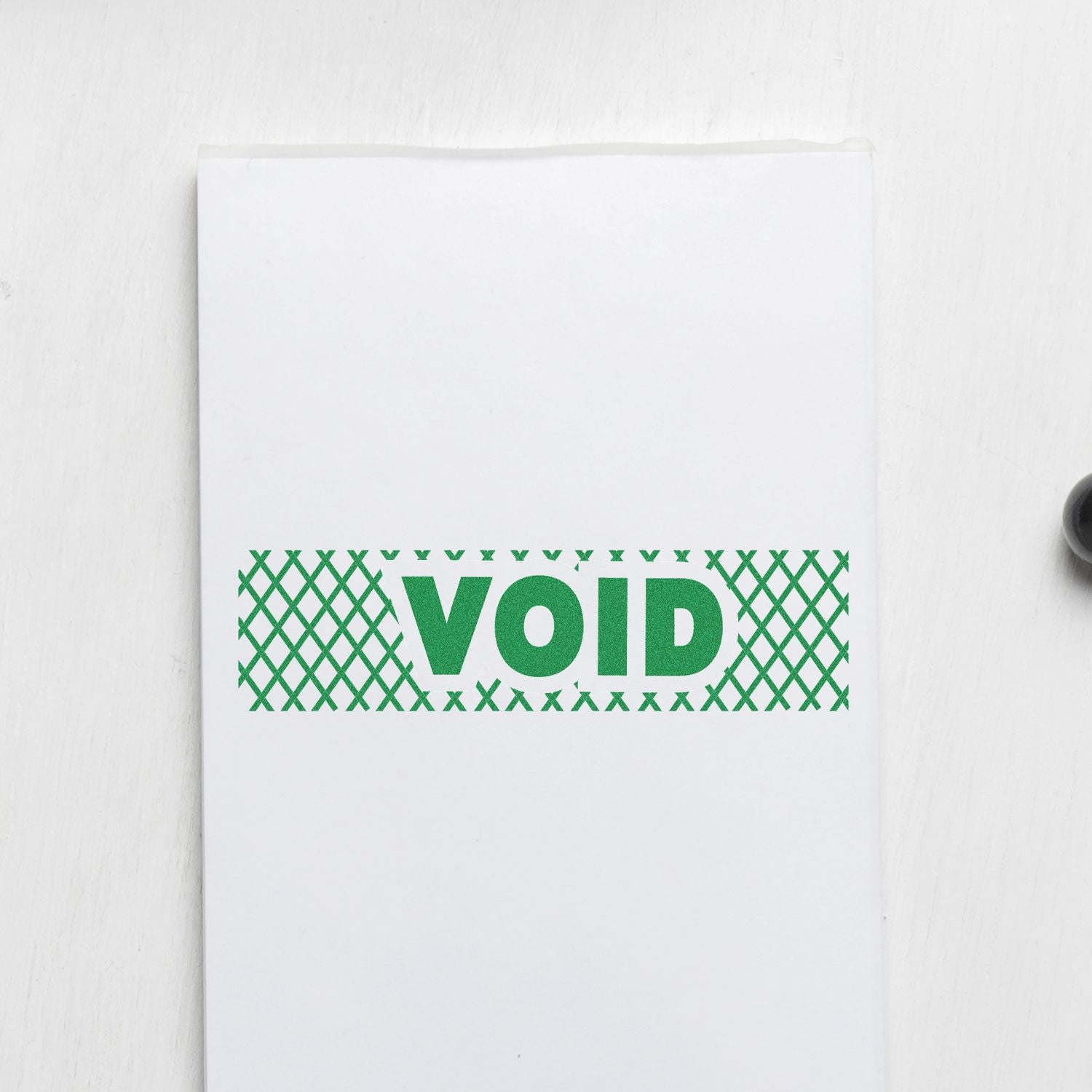 Green 'VOID' with strikelines rubber stamp impression on white paper, showing a clear and bold void message.