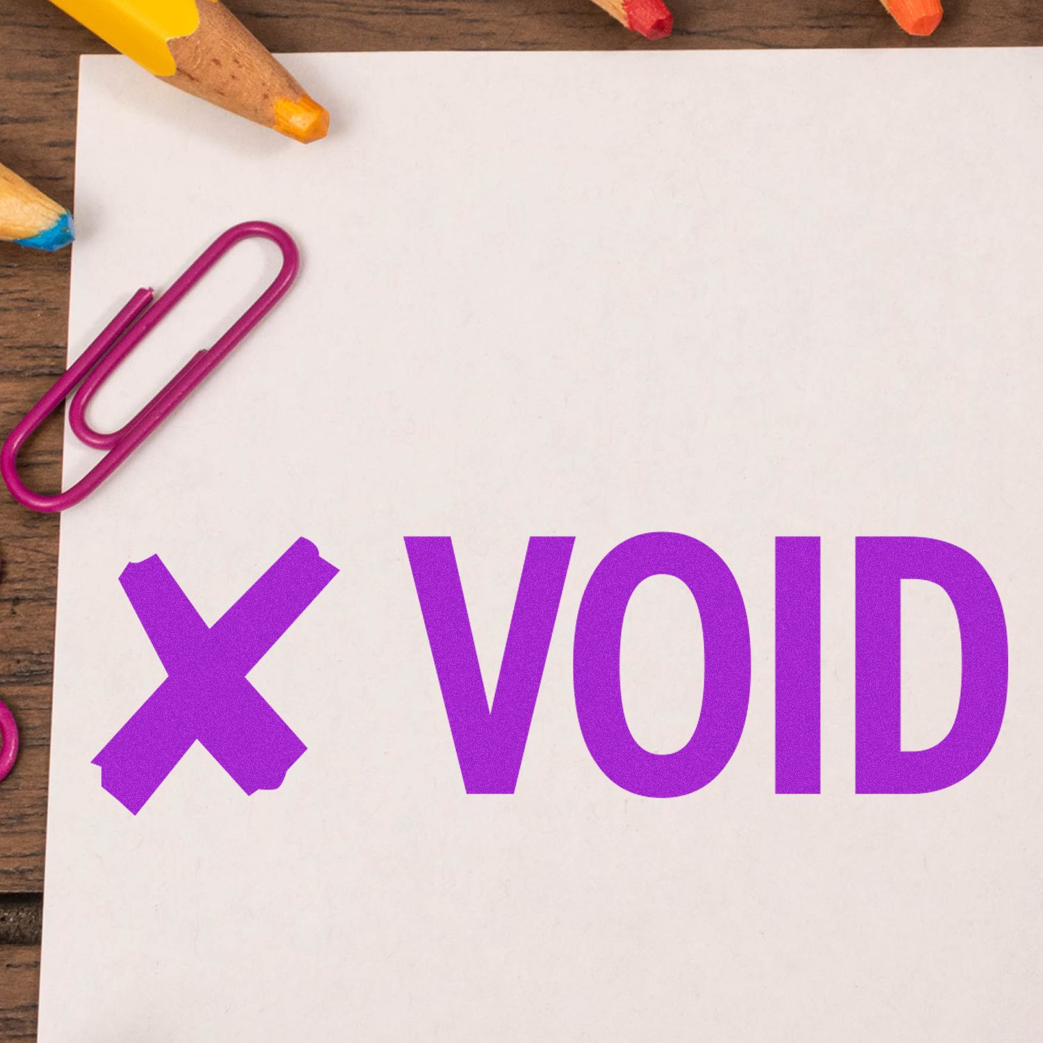 Large VOID with X rubber stamp in purple ink on white paper, surrounded by colorful pencils and a pink paperclip.