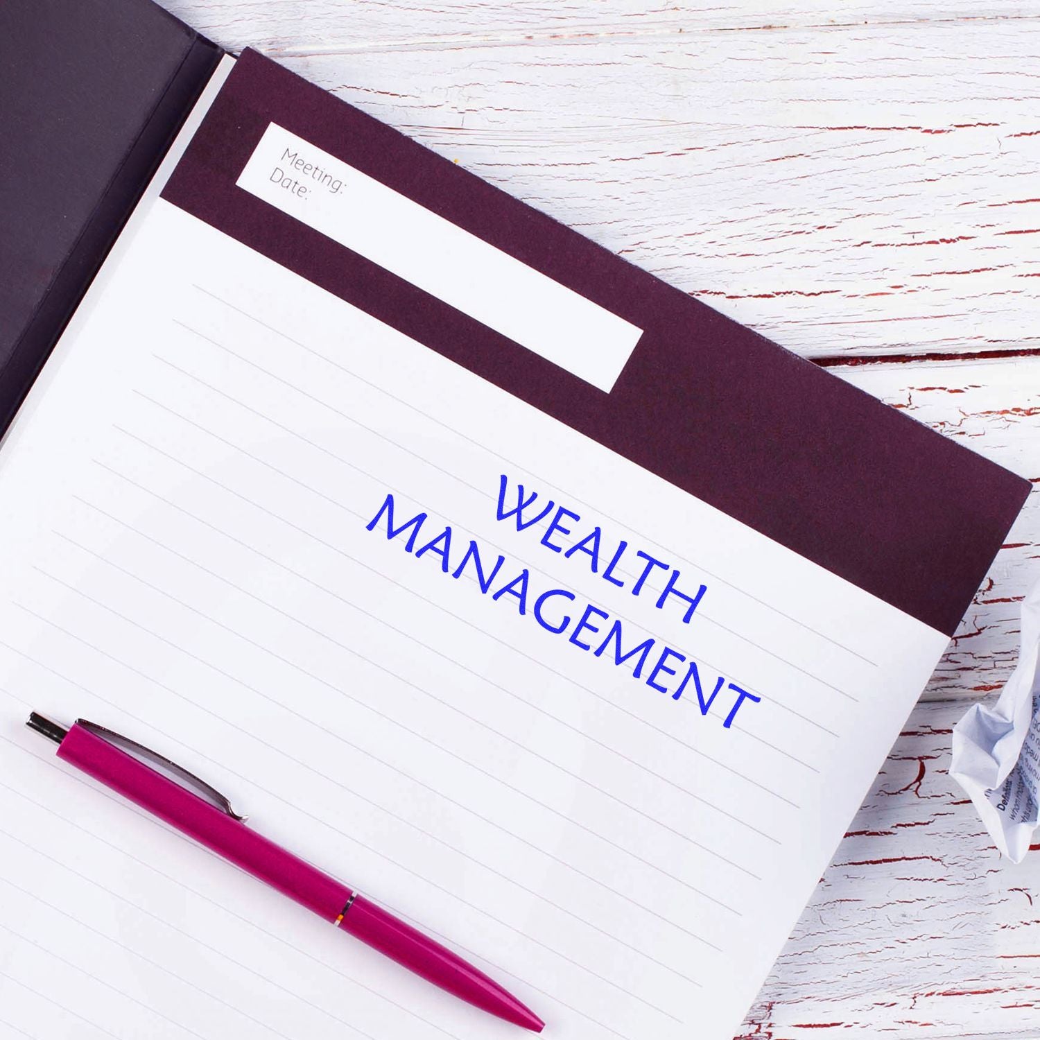 Notebook with Wealth Management stamped in blue using the Self Inking Wealth Management Stamp, alongside a pink pen on a white wooden desk.