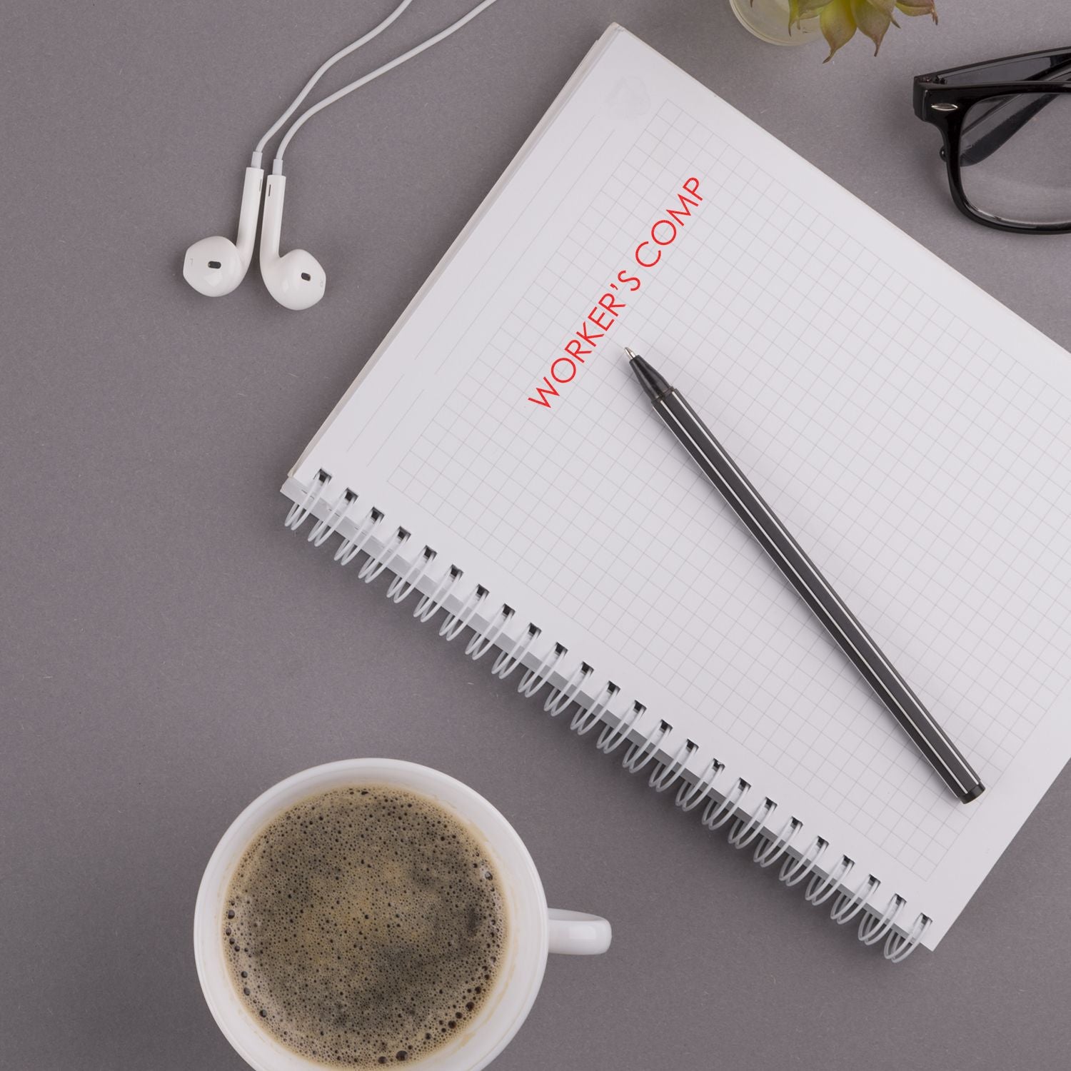 Large Pre-Inked Workers Comp Stamp used on a notebook with a pen, coffee cup, glasses, and earphones on a gray desk.