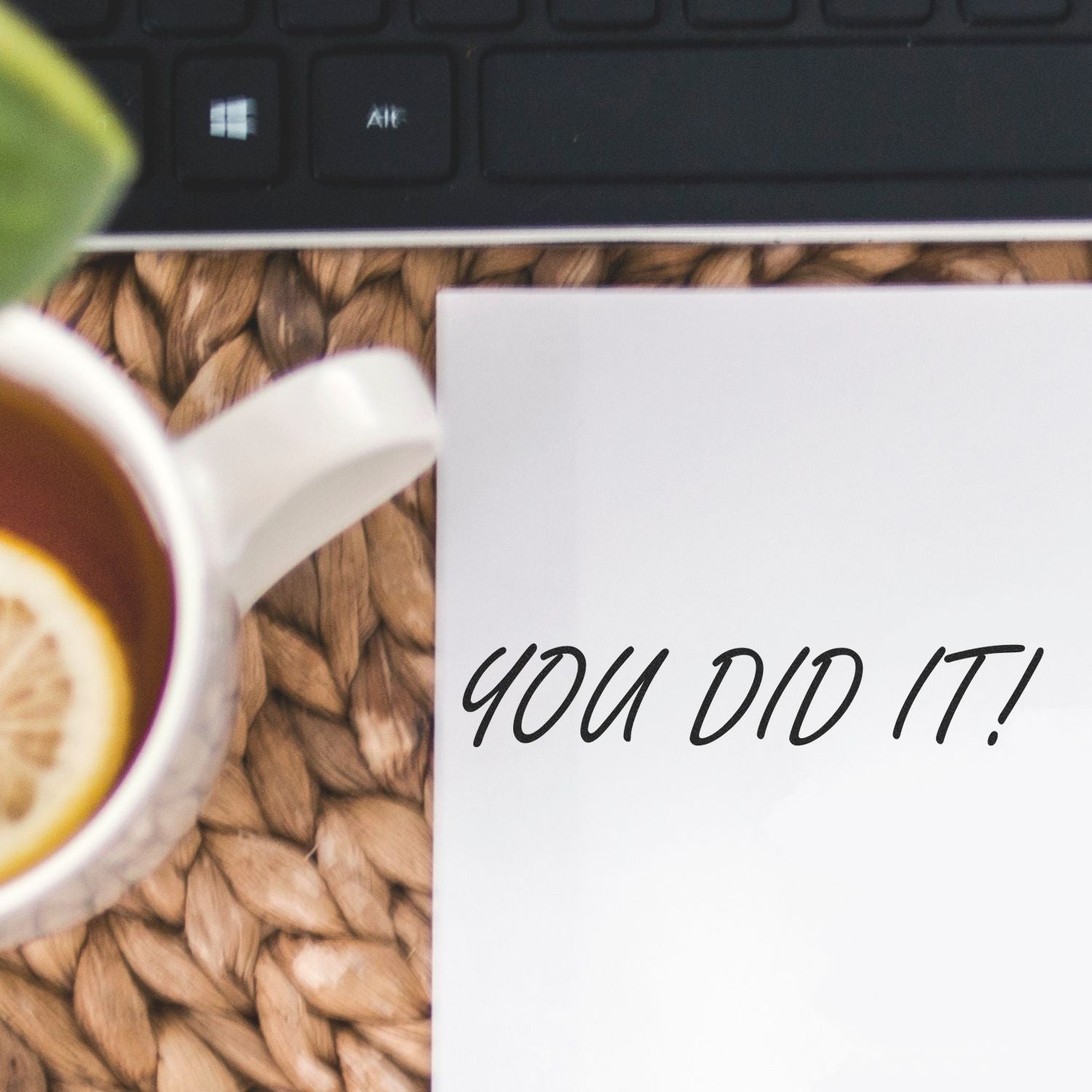 A Self Inking You Did It Stamp imprint on white paper, next to a cup of tea with lemon and a keyboard on a woven mat.