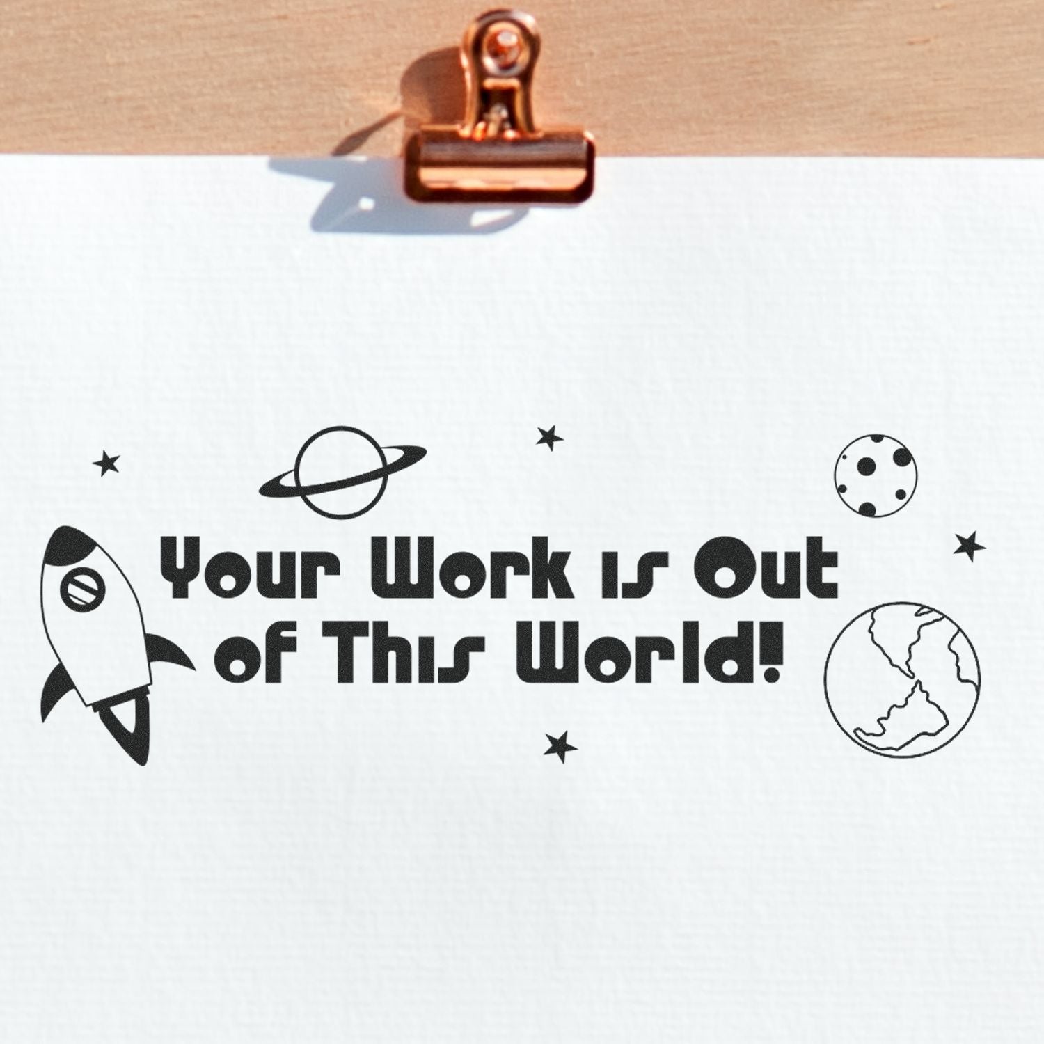 Large Your Work is Out of This World rubber stamp on white paper with space-themed illustrations, clipped to a wooden board.