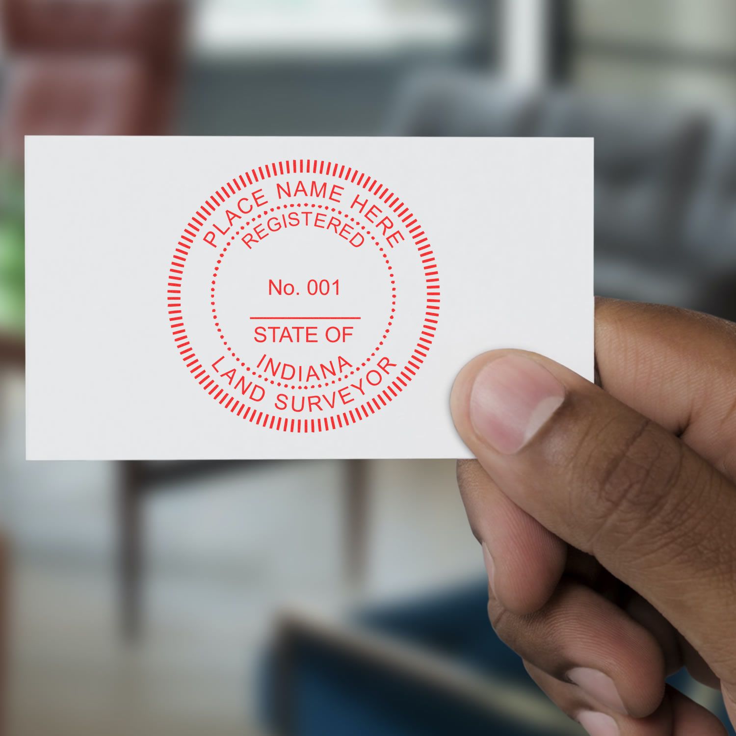 Hand holding a card stamped with the Self Inking Indiana Land Surveyor Stamp, displaying STATE OF INDIANA LAND SURVEYOR in red ink.