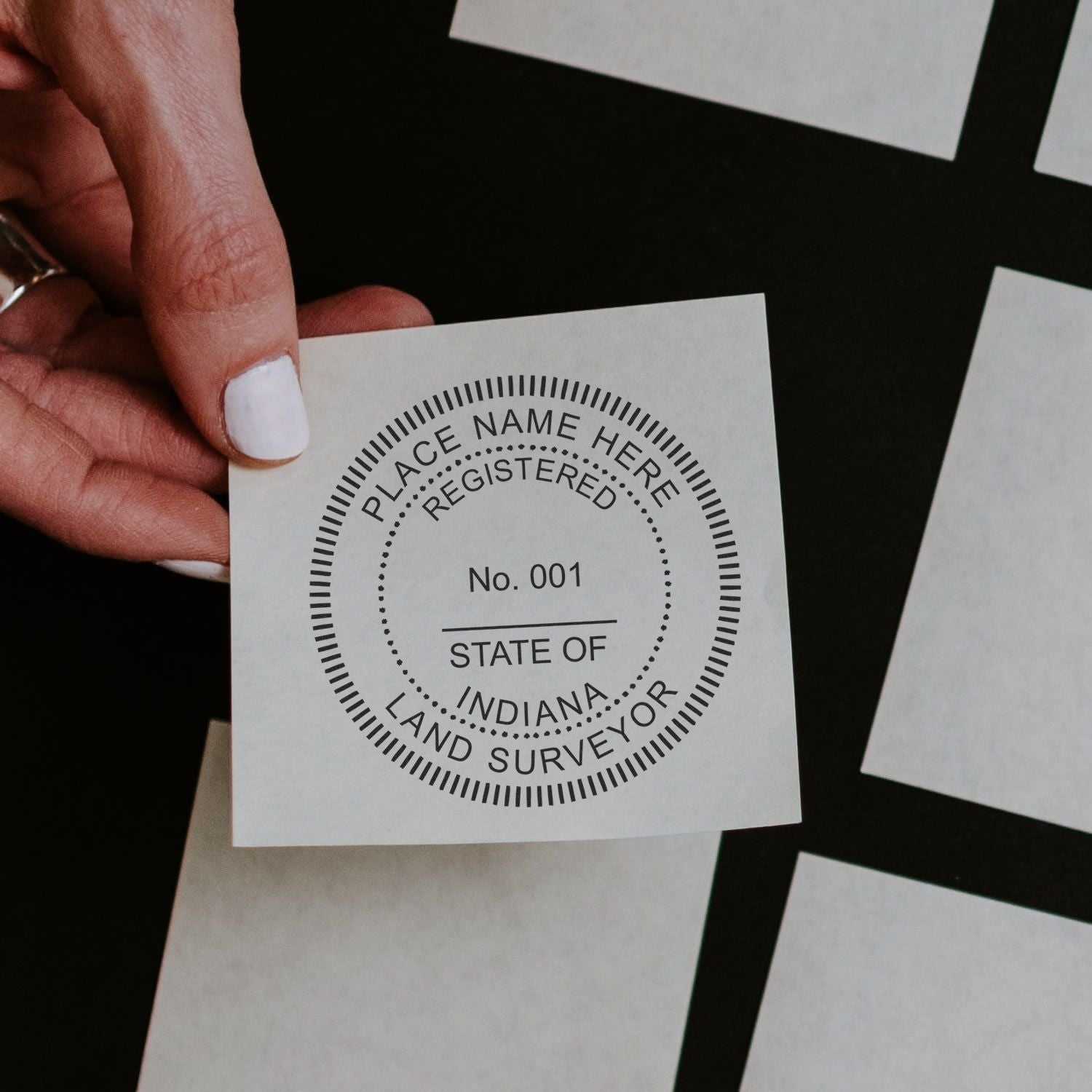 Hand holding a stamped paper with PLACE NAME HERE, REGISTERED, No. 001, STATE OF INDIANA, LAND SURVEYOR using Self Inking Indiana Land Surveyor Stamp.