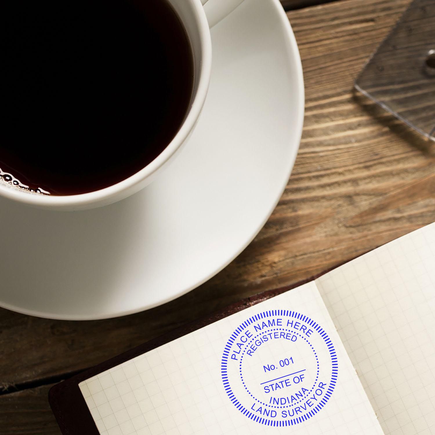 Self Inking Indiana Land Surveyor Stamp in use on a notebook, next to a cup of coffee on a wooden table.