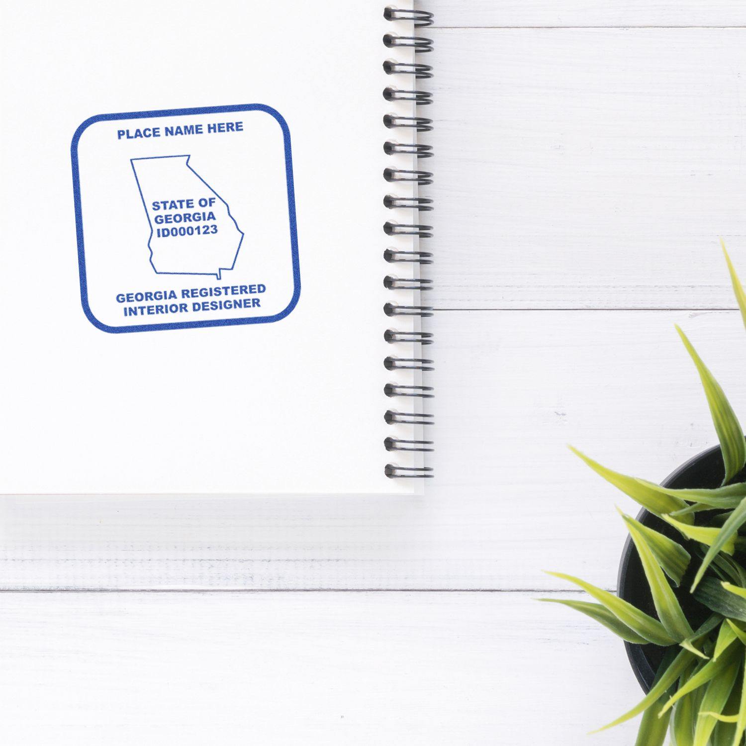 Interior Designer Regular Rubber Stamp of Seal stamped on a white notebook near a green plant on a white wooden surface.