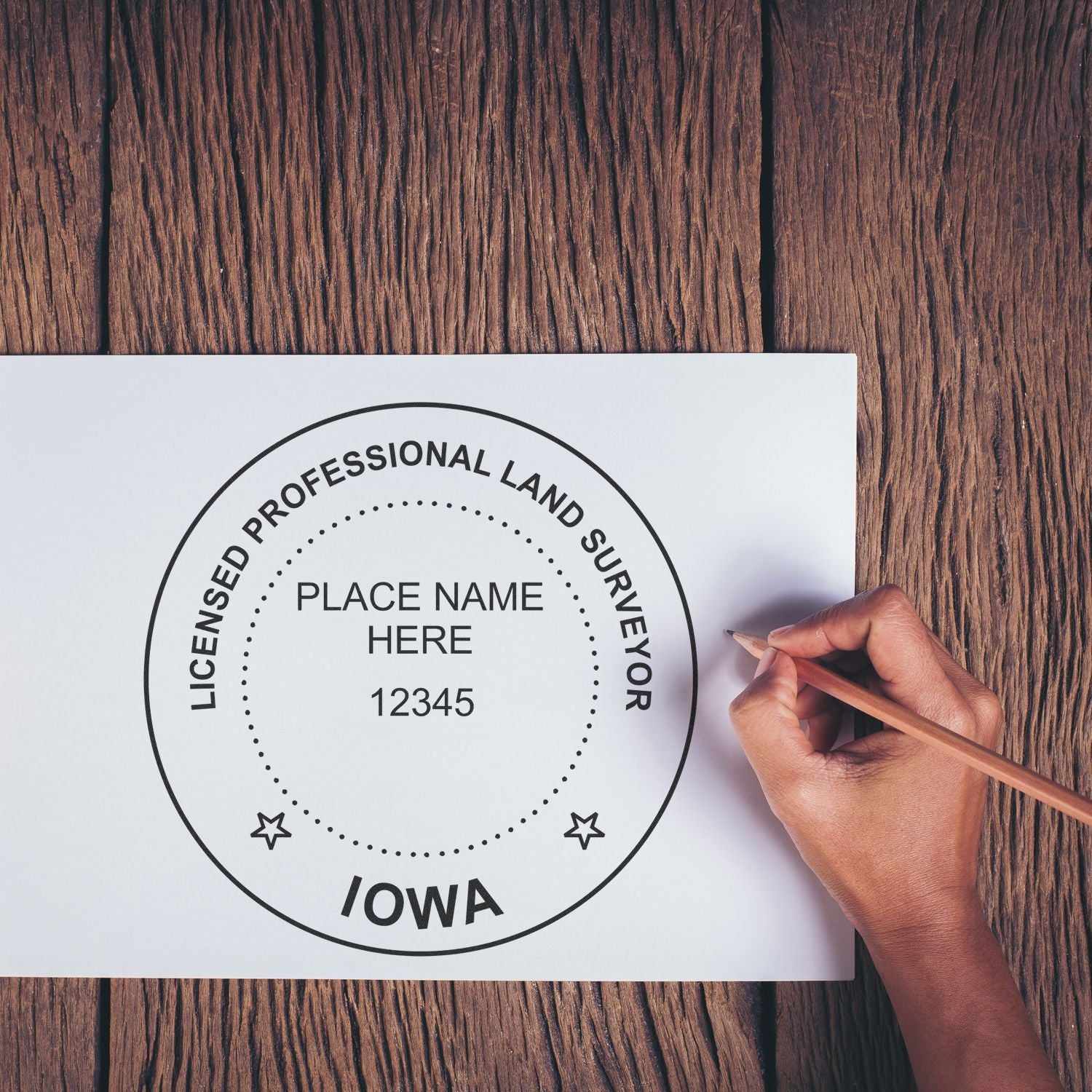 Hand using Premium MaxLight Pre-Inked Iowa Surveyors Stamp on white paper, wooden table background.