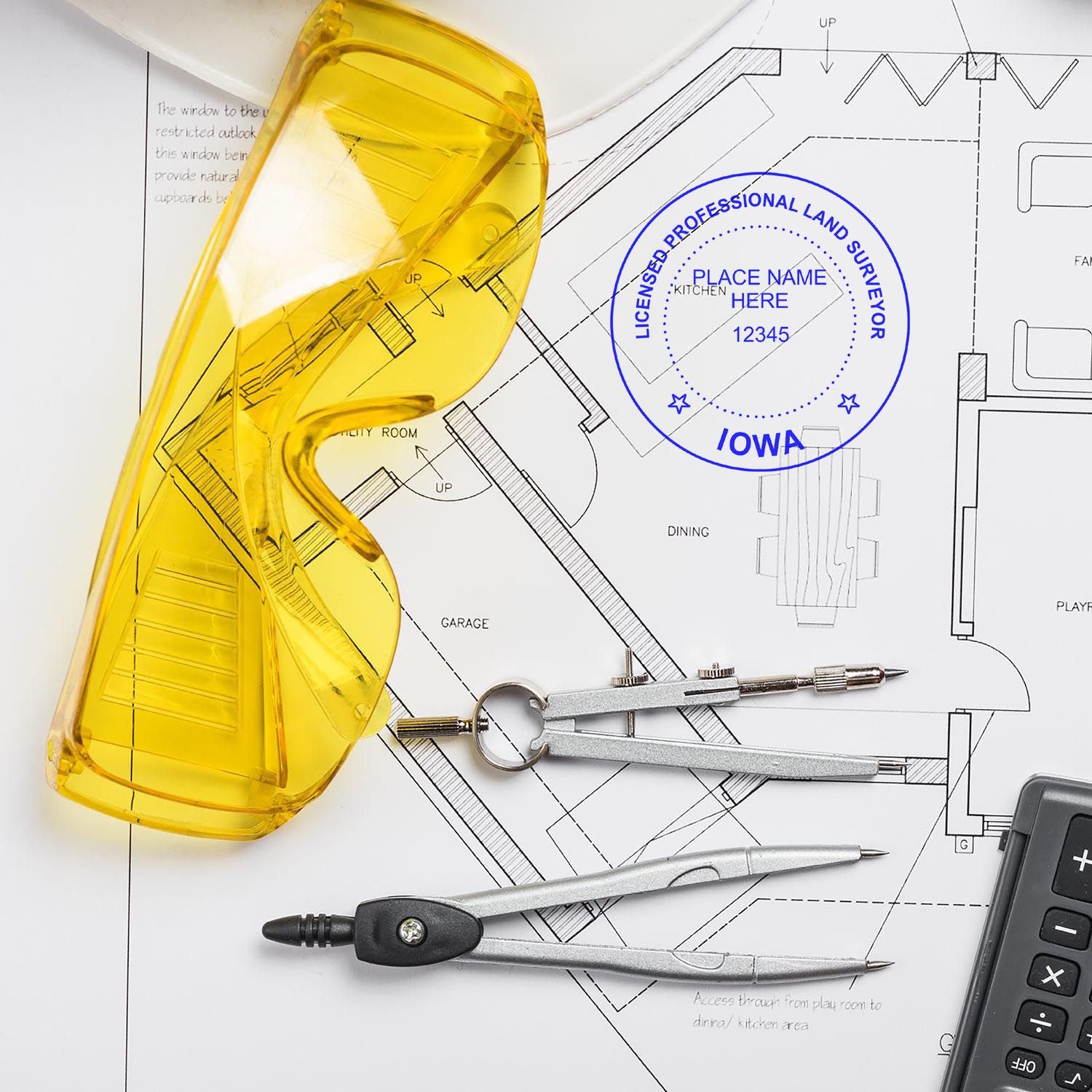 Yellow safety glasses, compass, and Premium MaxLight Pre-Inked Iowa Surveyors Stamp on architectural plans with a calculator in the background.