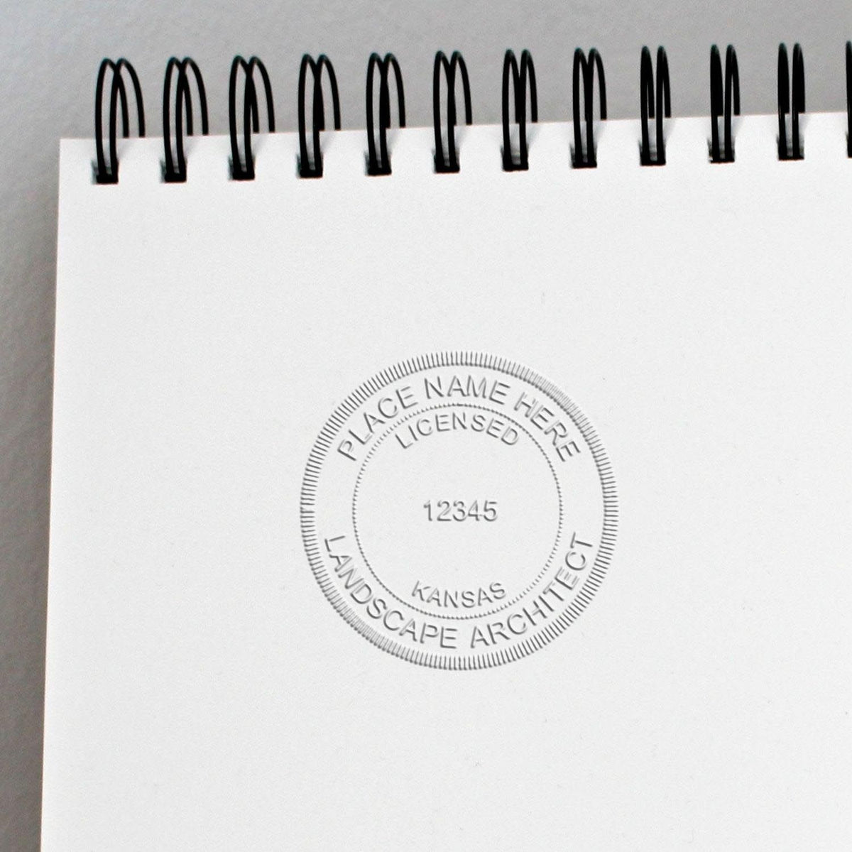 An in use photo of the Gift Kansas Landscape Architect Seal showing a sample imprint on a cardstock