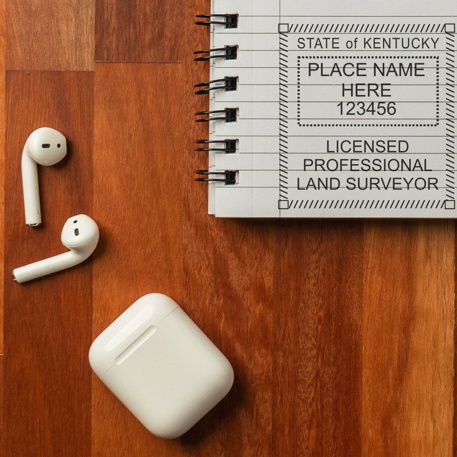 Premium MaxLight Pre-Inked Kentucky Surveyors Stamp on a notebook, with wireless earbuds and case on a wooden surface.