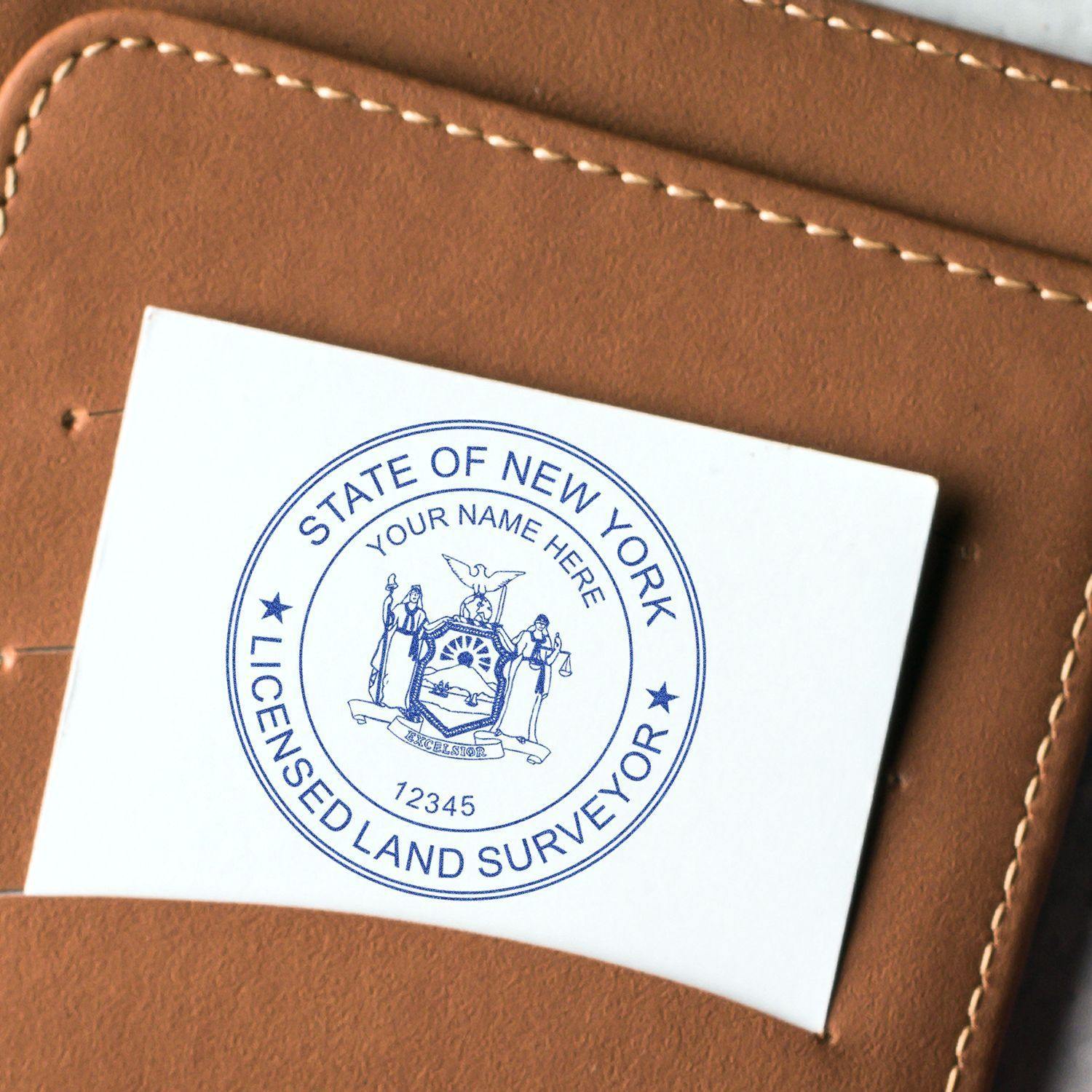 Land Surveyor Regular Rubber Stamp of Seal with State of New York Licensed Land Surveyor text on a white card, placed on a brown leather surface.