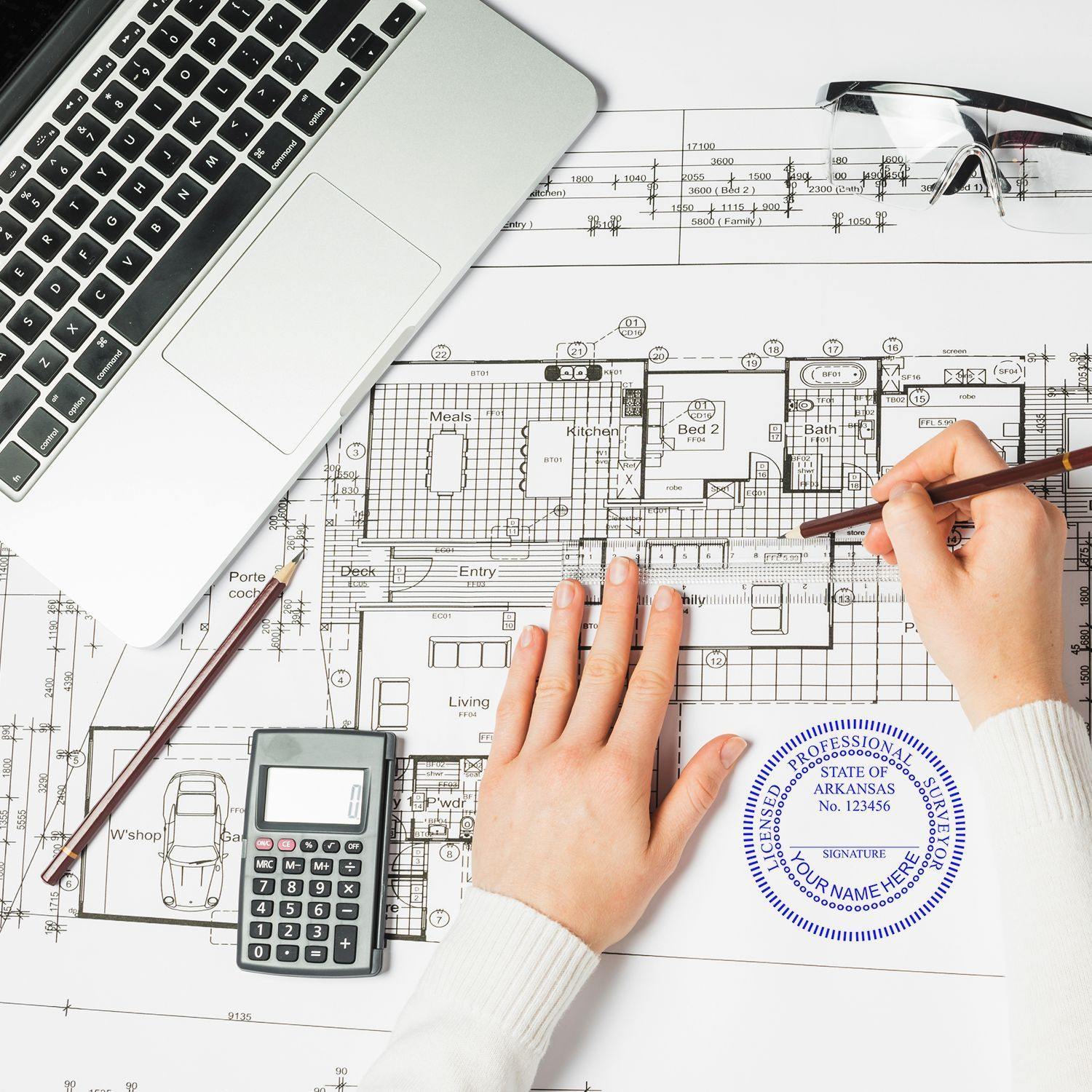 Hands using Land Surveyor Regular Rubber Stamp of Seal on architectural plans, with a laptop, calculator, and glasses nearby.