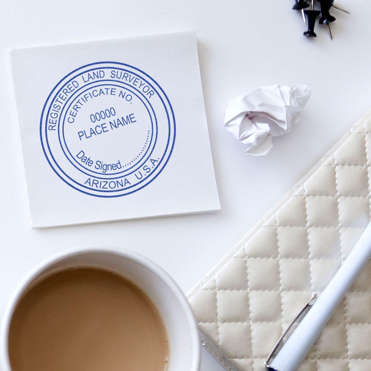 Xstamper Land Surveyor Pre-Inked Rubber Stamp of Seal on white paper, surrounded by a coffee cup, pen, and crumpled paper.