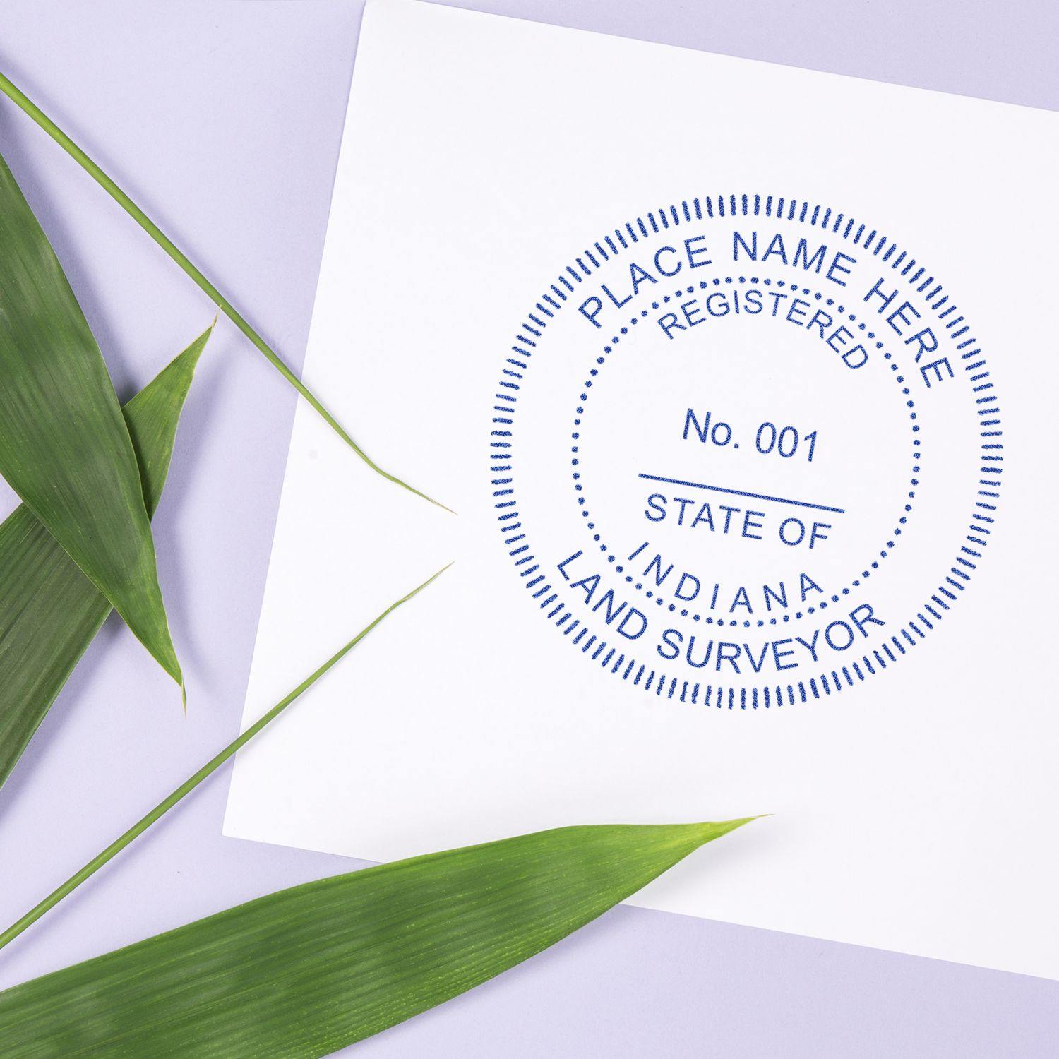 Land Surveyor MaxLight Pre Inked Rubber Stamp of Seal in use, stamping a document with green leaves beside it.