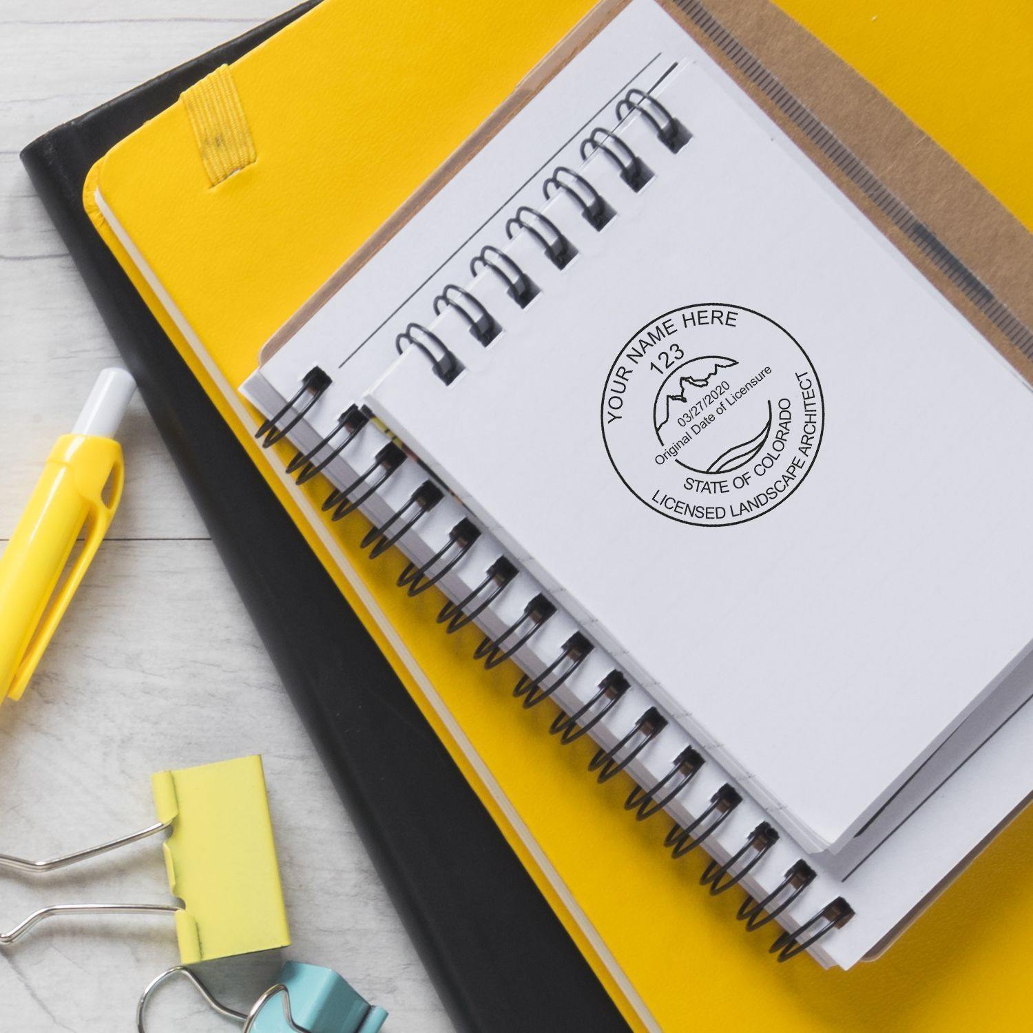 Landscape Architect Regular Rubber Stamp of Seal stamped on a white notebook, placed on top of yellow folders with a pen and binder clips nearby.