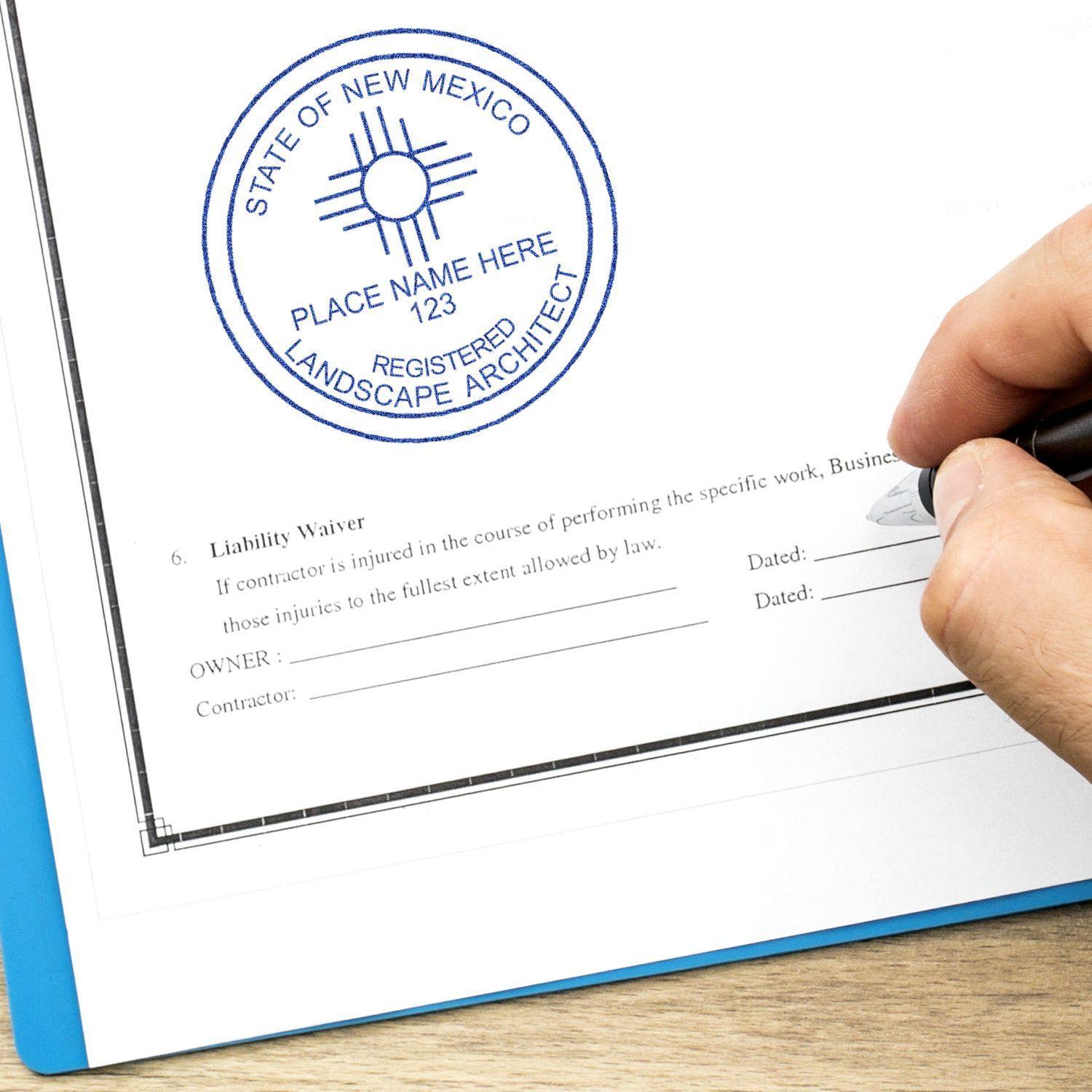 Hand holding pen next to a blue Landscape Architect Regular Rubber Stamp of Seal imprint on a document, reading State of New Mexico.