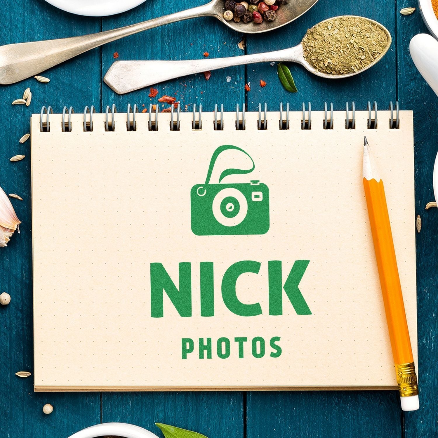 A Custom Rubber Stamp Size 6 x 6 is used to stamp NICK PHOTOS with a camera icon on a spiral notebook, surrounded by spices and a pencil.