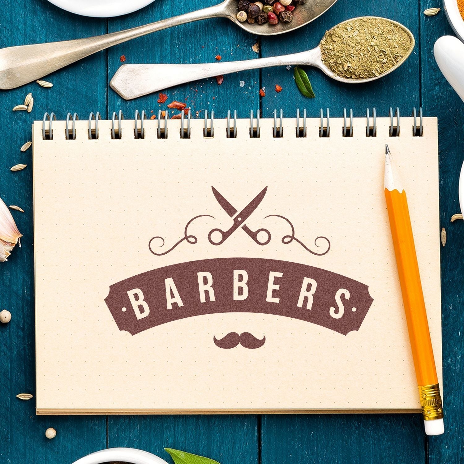 Notebook with Barbers logo stamped using Custom Rubber Stamp Size 5 x 9, surrounded by a pencil, spices, and utensils on a blue wooden table.