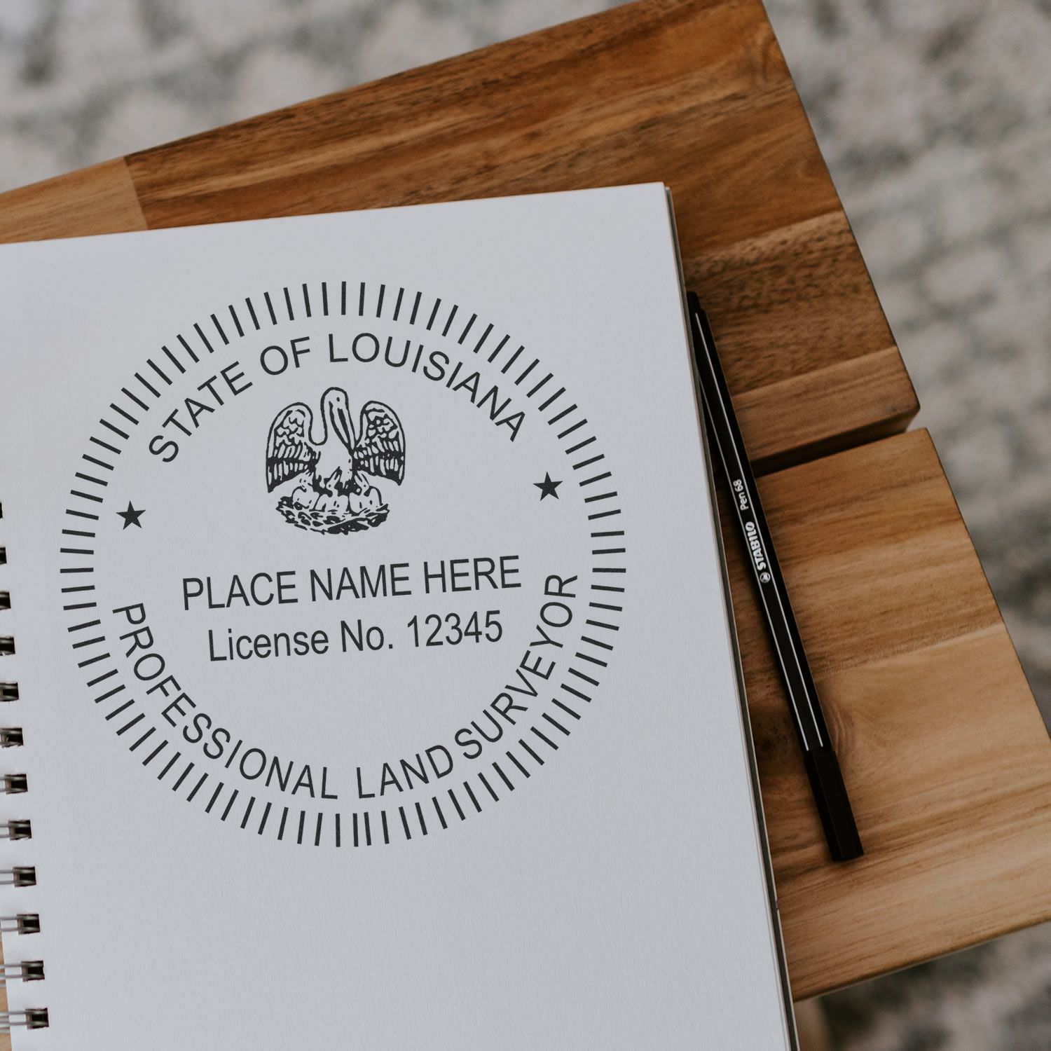 Louisiana Land Surveyor Seal Stamp, LA PLS Stamp on a notebook with a pen beside it on a wooden table.