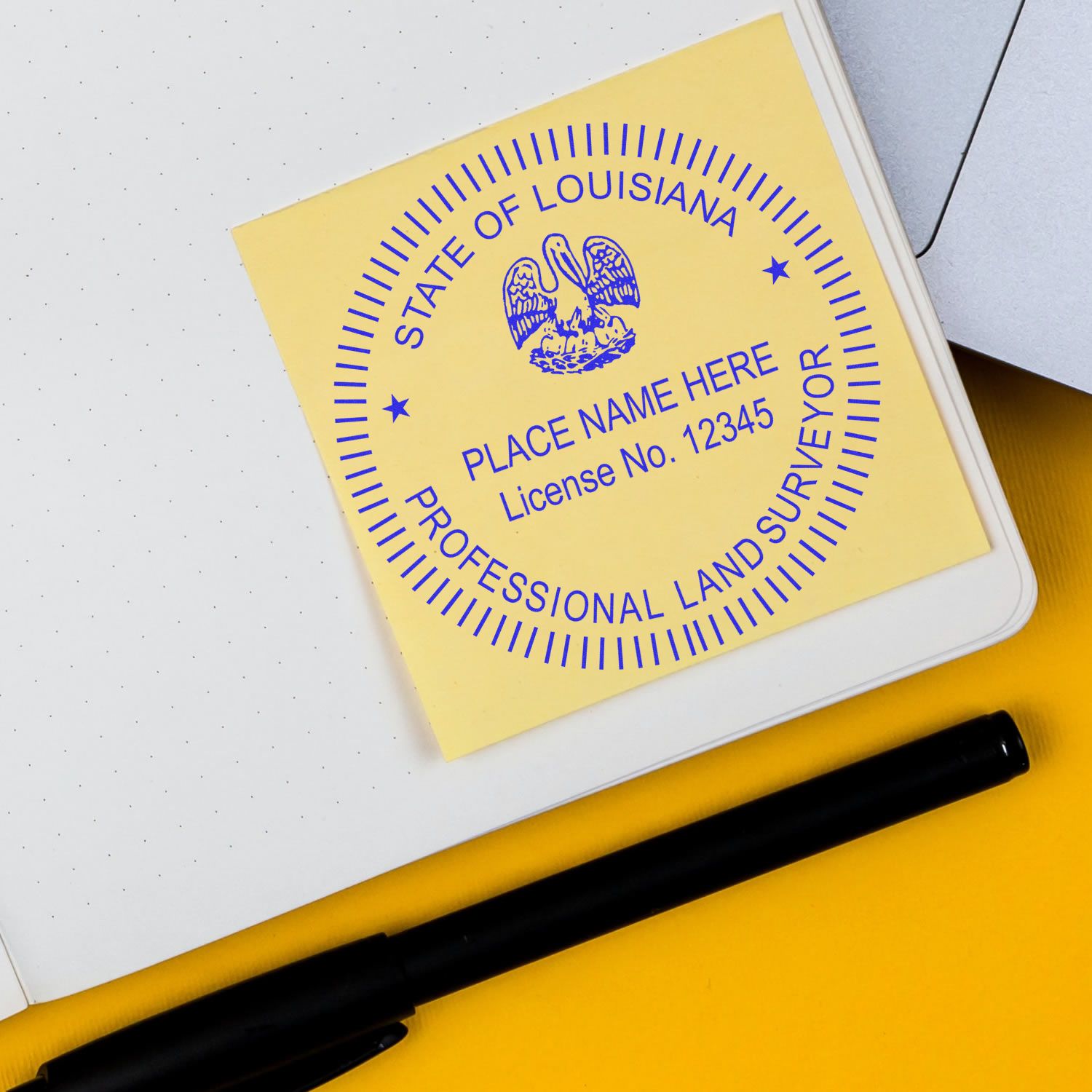 Louisiana Land Surveyor Seal Stamp, LA PLS Stamp on a yellow sticky note beside a black pen and a notebook.