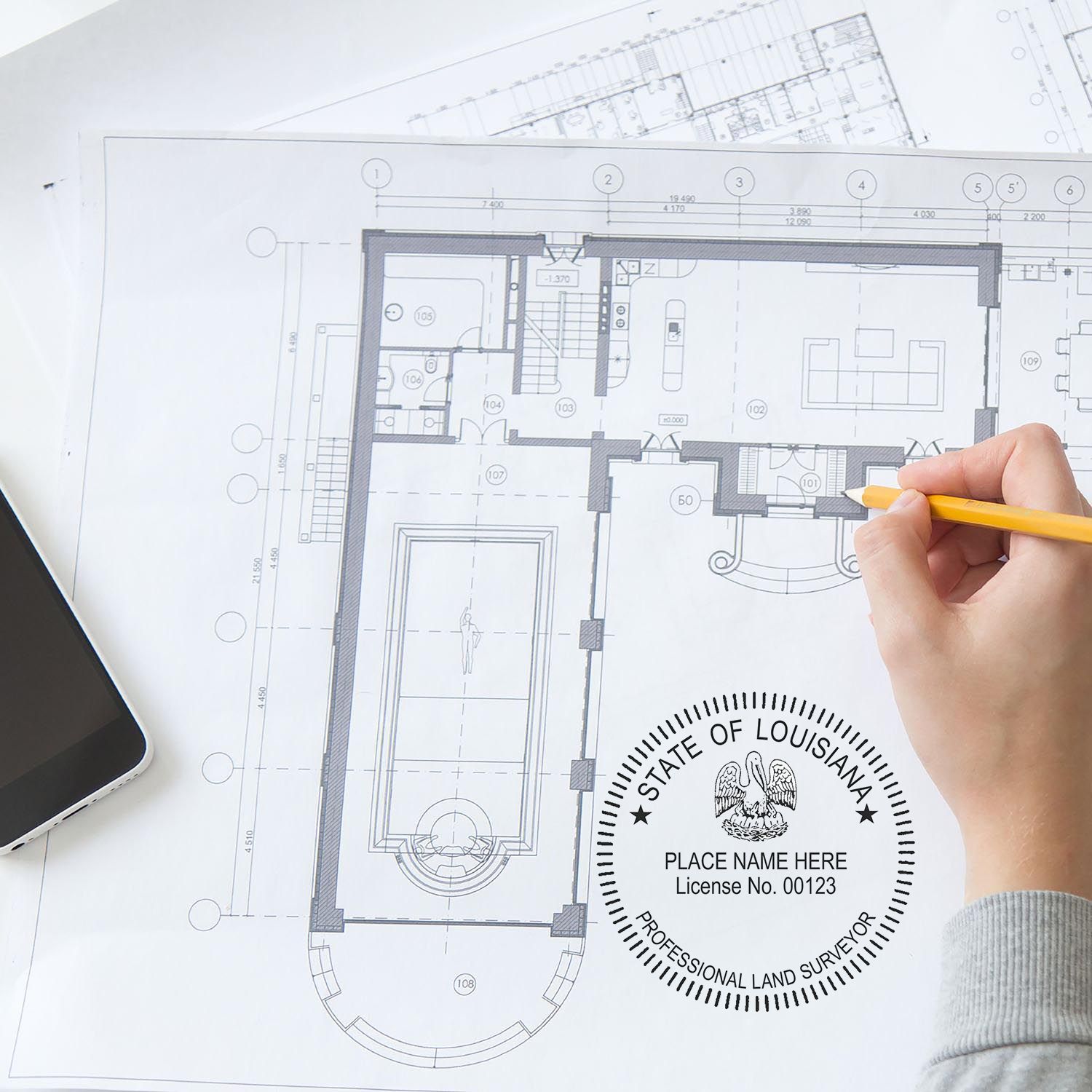 Hand holding pencil over architectural blueprint with Self Inking Louisiana Land Surveyor Stamp imprint visible on the paper.