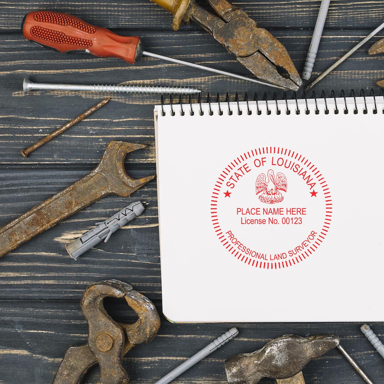 Self Inking Louisiana Land Surveyor Stamp imprint on a spiral notebook, surrounded by various rusty tools on a wooden surface.