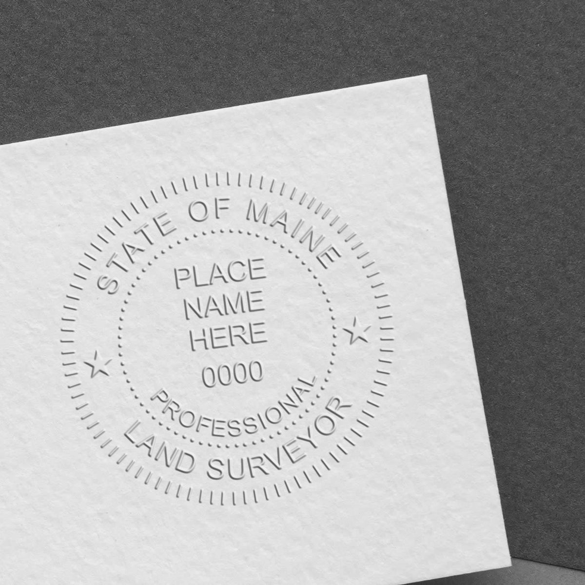 A lifestyle photo showing a stamped image of the Extended Long Reach Maine Surveyor Embosser on a piece of paper