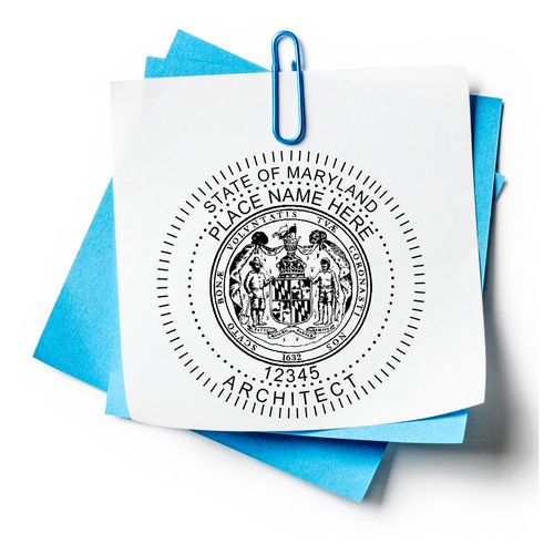 Premium MaxLight Pre-Inked Maryland Architectural Stamp on white paper with blue sheets underneath, secured by a blue paperclip.