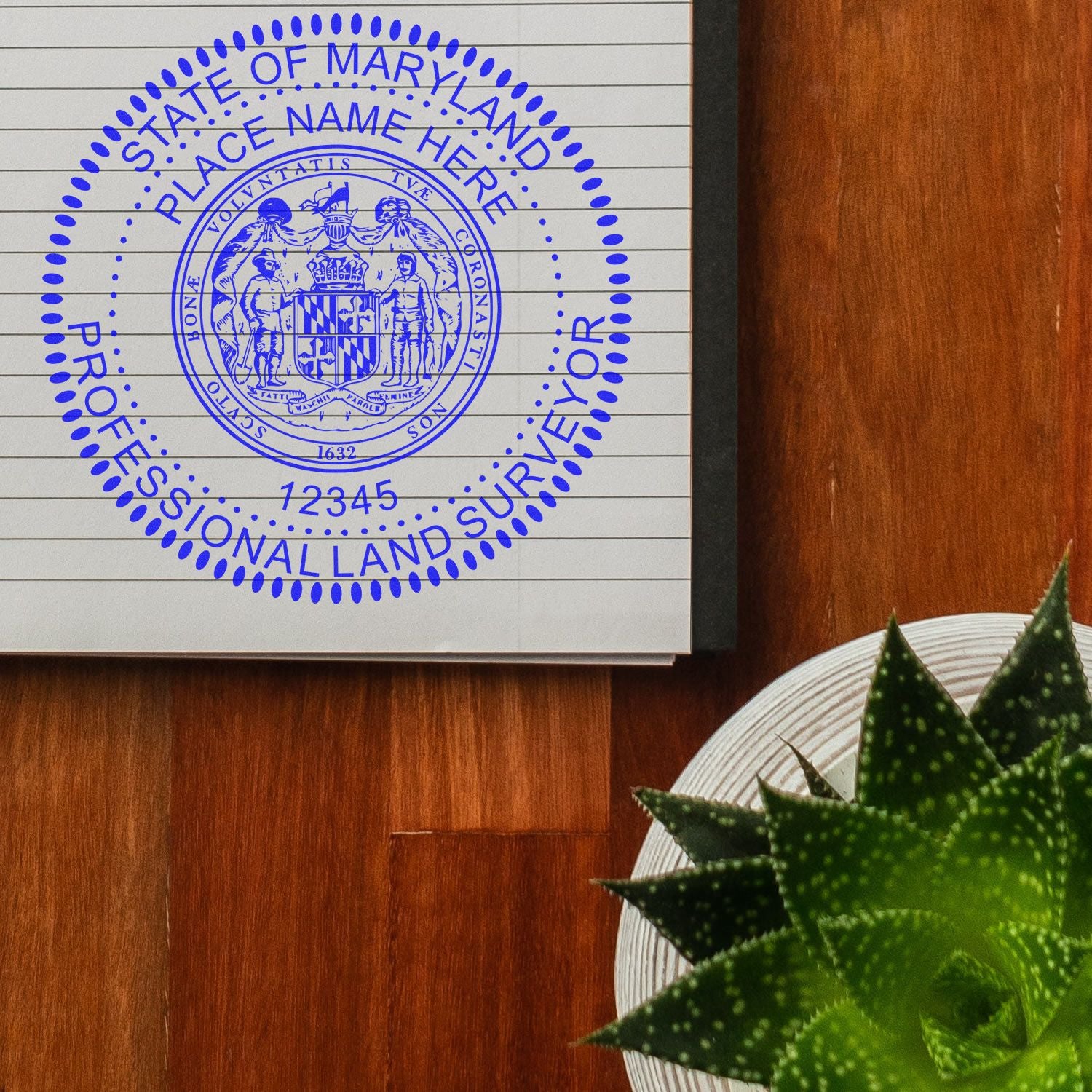 Premium MaxLight Pre-Inked Maryland Surveyors Stamp in blue ink on a notebook, placed on a wooden table next to a green succulent plant.