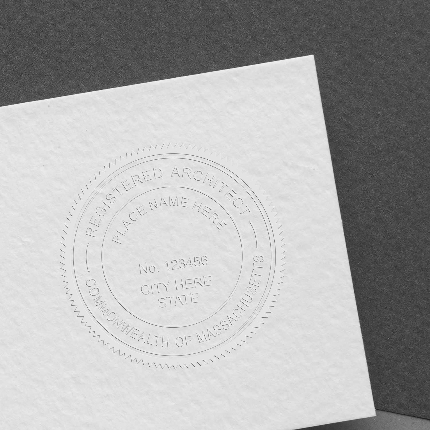 A close-up of a white paper embossed with a seal using the Architect Hybrid Seal Embosser, showing the text Registered Architect, Commonwealth of Massachusetts and placeholders for name, number, city, and state.