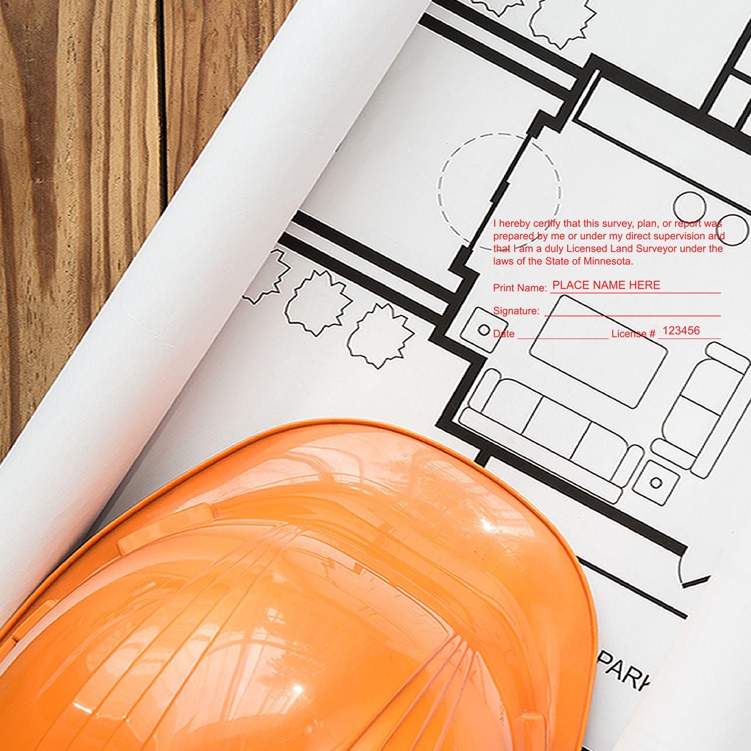 Self Inking Minnesota Land Surveyor Stamp in use on a rolled blueprint with an orange hard hat placed on a wooden surface.