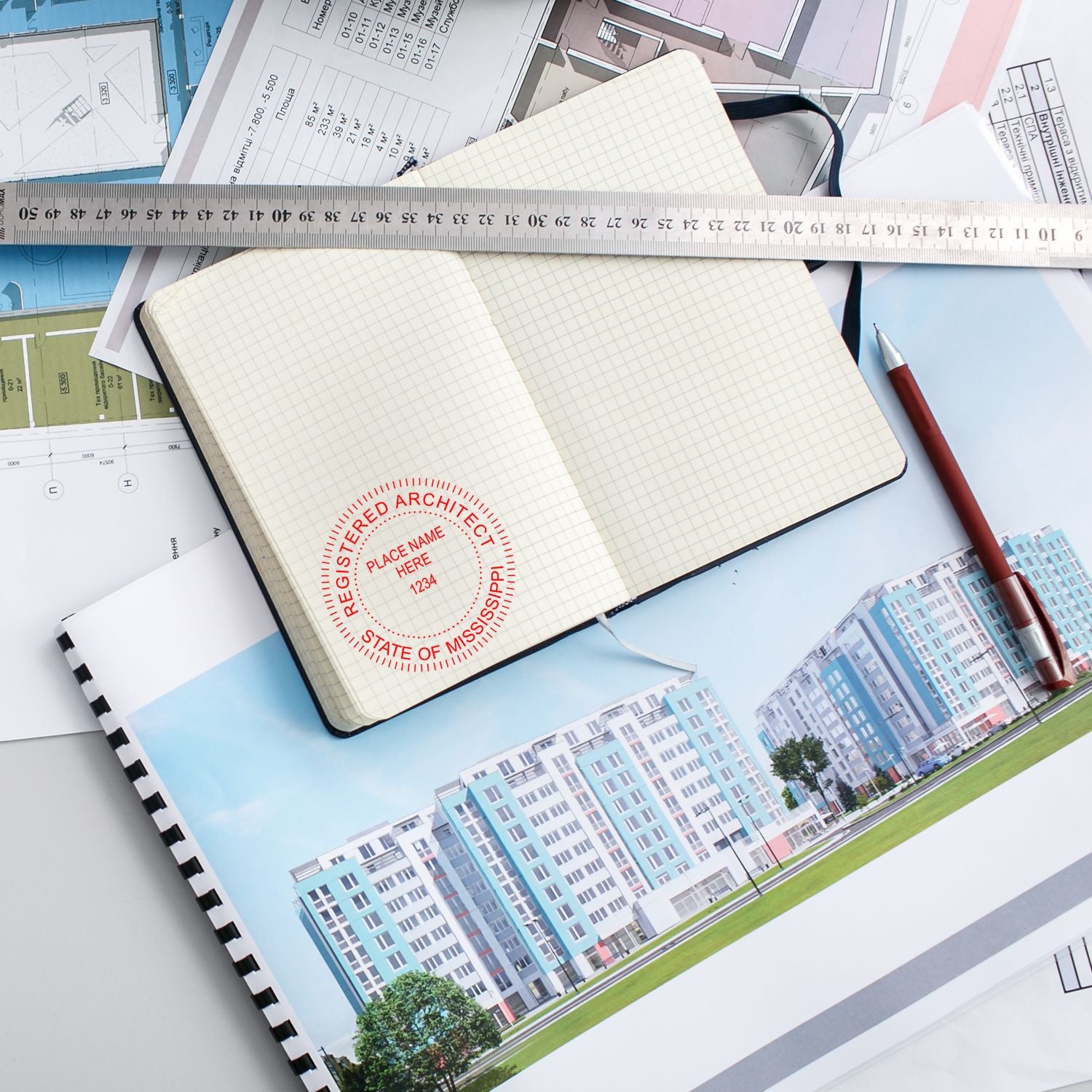 Mississippi Architect Seal Stamp on an open notebook, surrounded by architectural plans, a ruler, a pen, and a building photo.