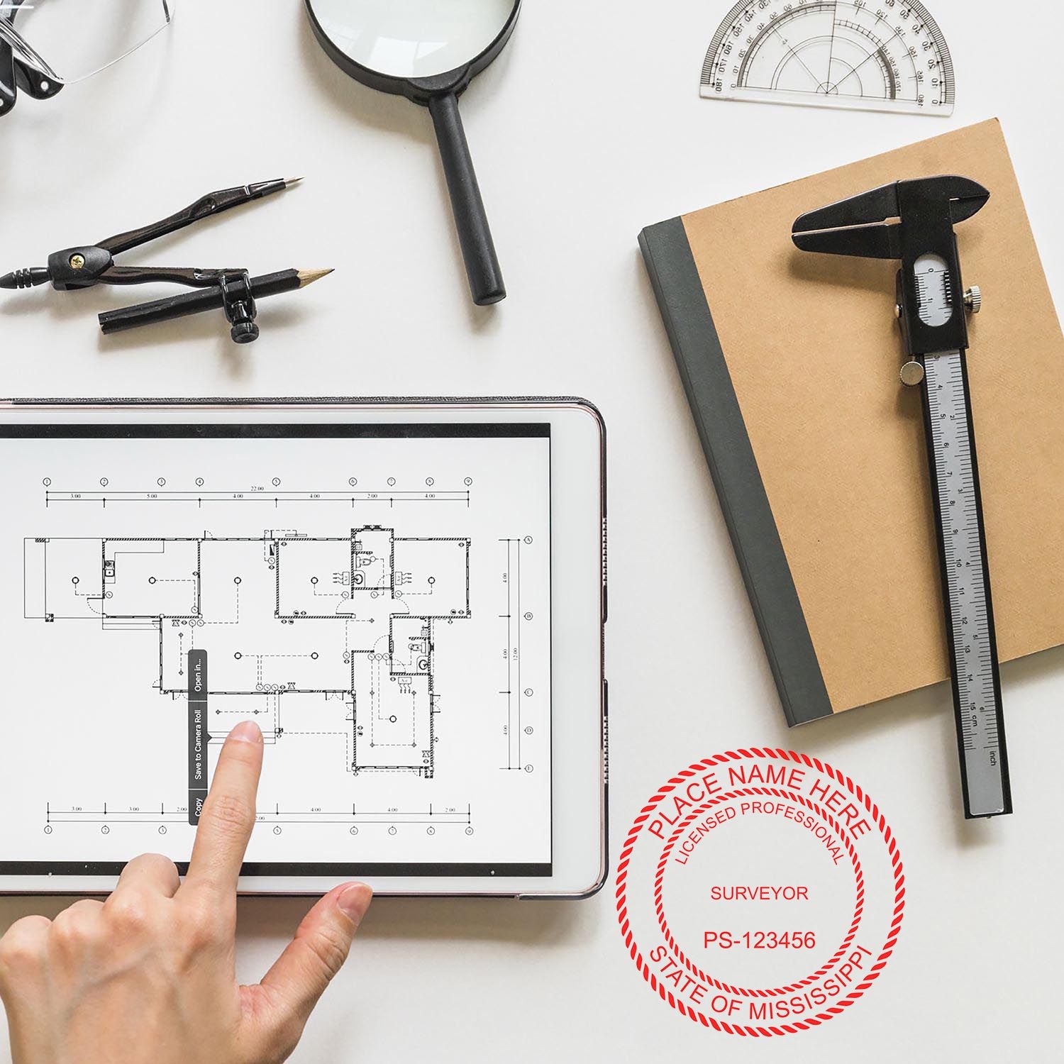 A person points to a digital blueprint on a tablet, surrounded by surveying tools and a notebook with a Digital Mississippi Land Surveyor Stamp.