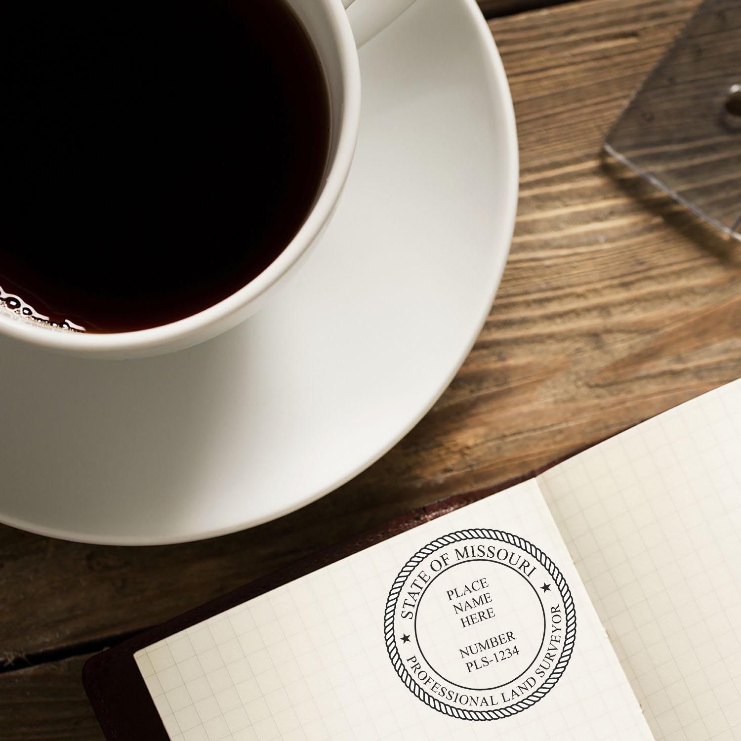 Self Inking Missouri Land Surveyor Stamp in use on a notebook, next to a cup of coffee on a wooden table.