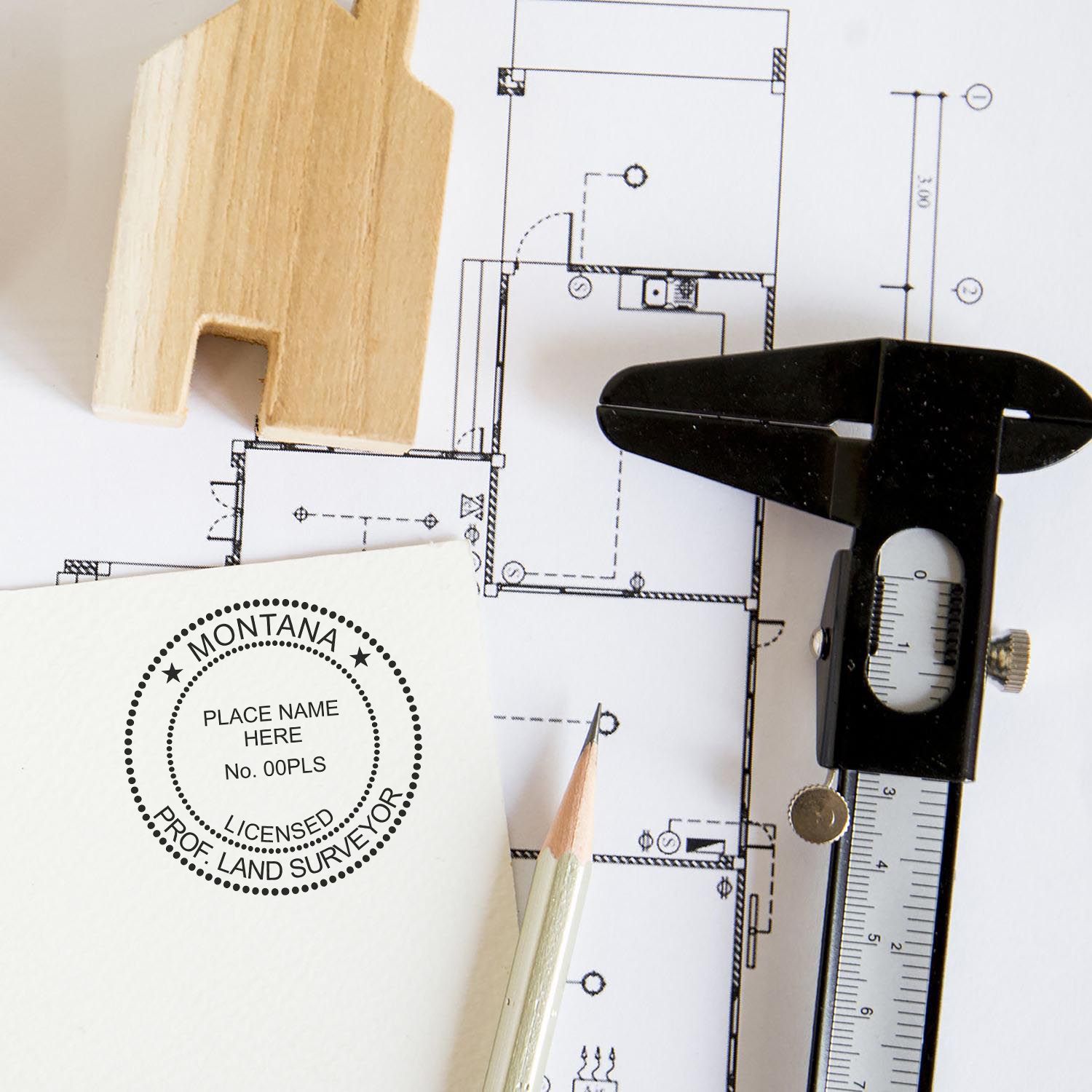 Montana Land Surveyor Seal Stamp, MT PLS Stamp on paper with architectural plans, a pencil, a caliper, and a wooden house model.