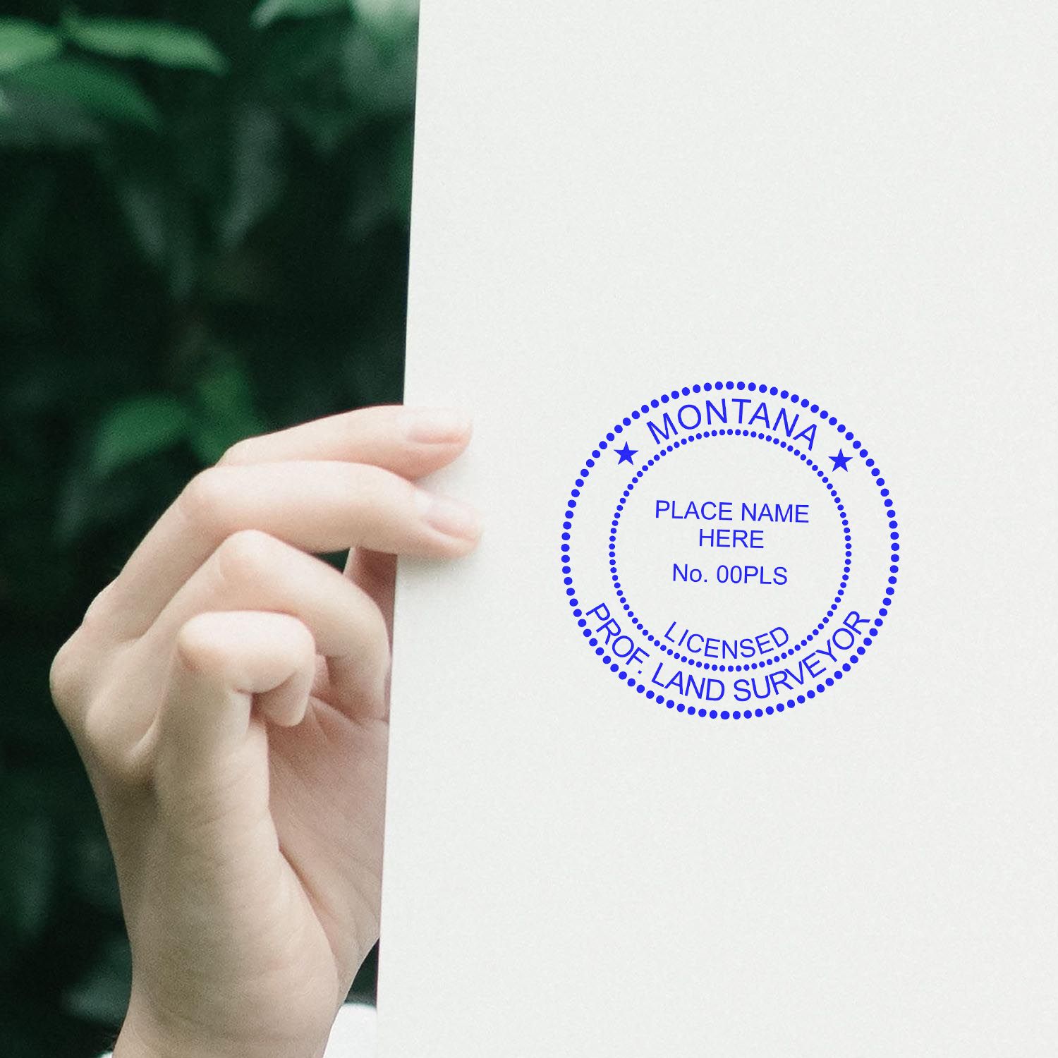 Hand holding paper stamped with Premium MaxLight Pre-Inked Montana Surveyors Stamp, showing a blue circular seal for licensed professional land surveyors.