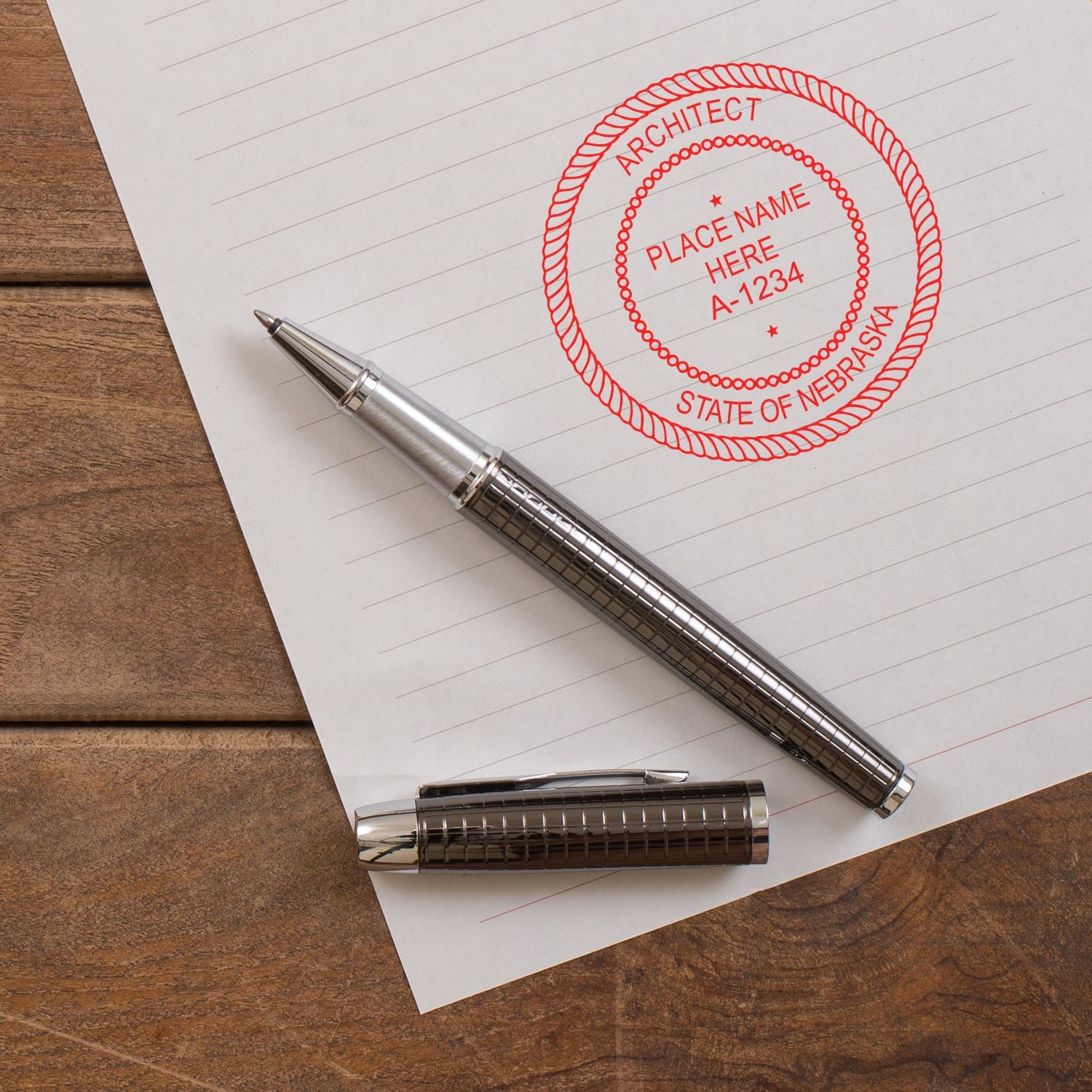 Self Inking Nebraska Architect Stamp in red ink on paper, next to a silver pen and pen cap on a wooden desk.