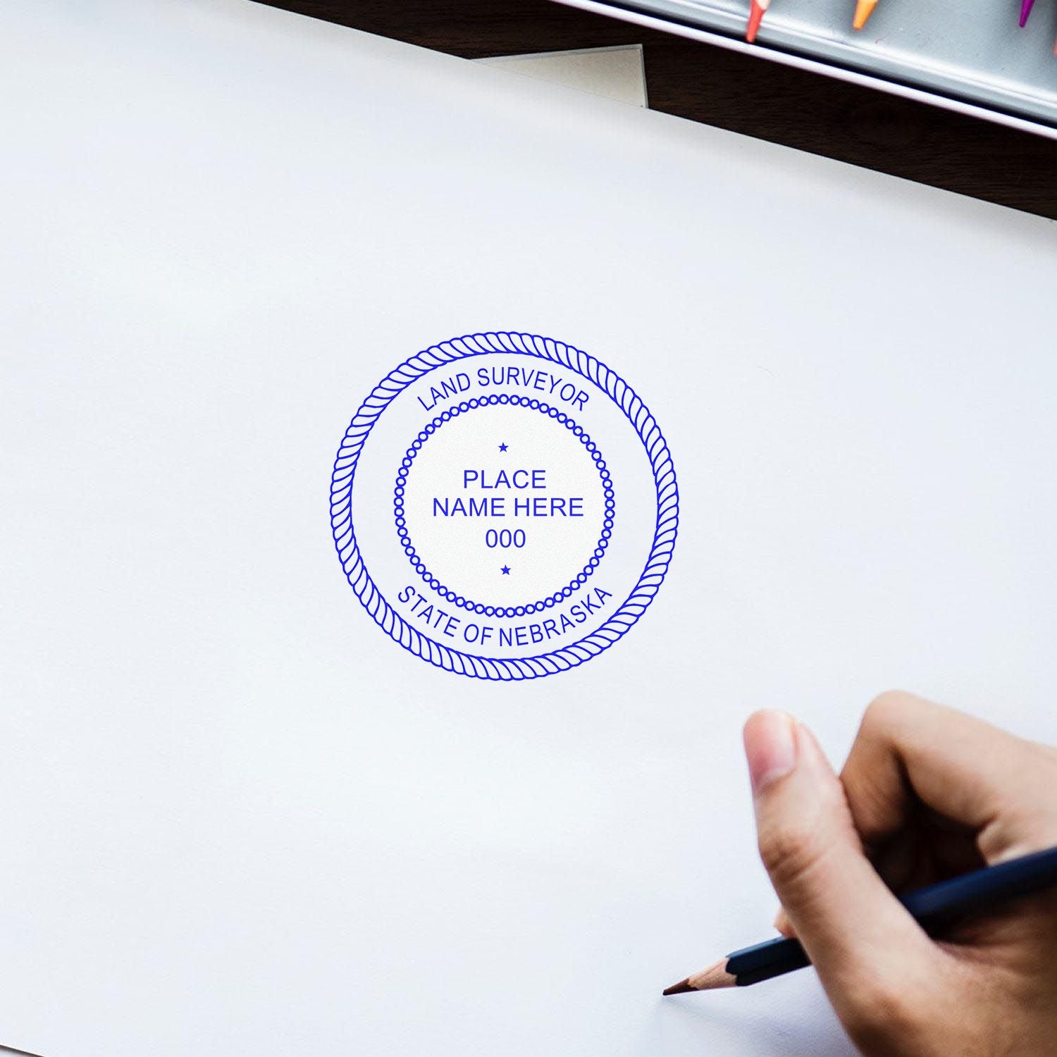 Hand using Self Inking Nebraska Land Surveyor Stamp on white paper, with blue ink imprint showing State of Nebraska Land Surveyor seal.