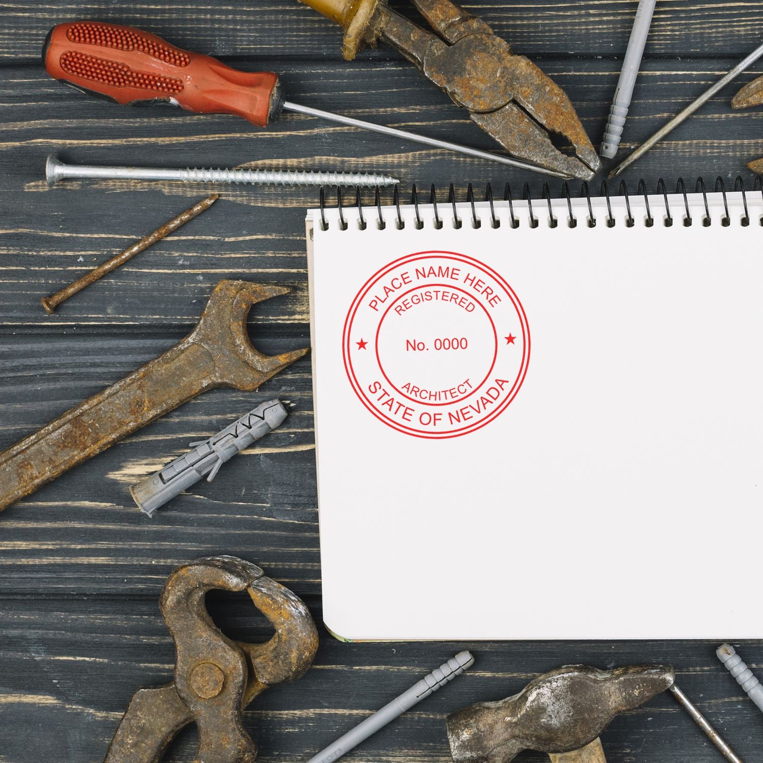 Self Inking Nevada Architect Stamp on a blank notebook page surrounded by various rusty tools on a wooden surface.