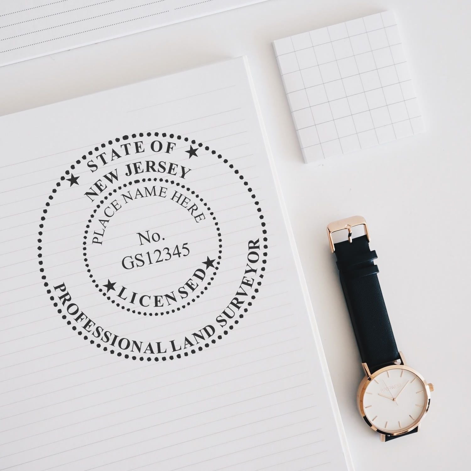 Digital New Jersey Land Surveyor Stamp, Electronic Seal for New Jersey Land Surveyor on a notepad beside a watch and a grid notepad.