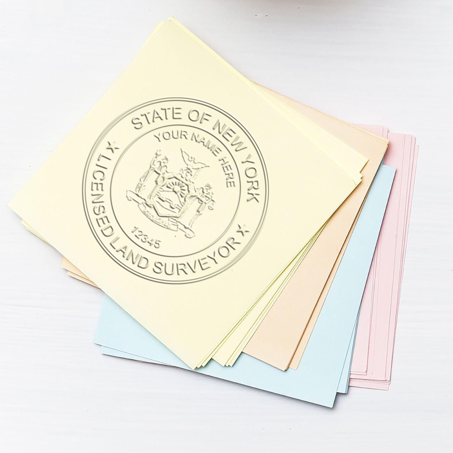 Land Surveyor Pink Hybrid Handheld Embosser imprint on a stack of pastel-colored papers, showing a New York licensed land surveyor seal.