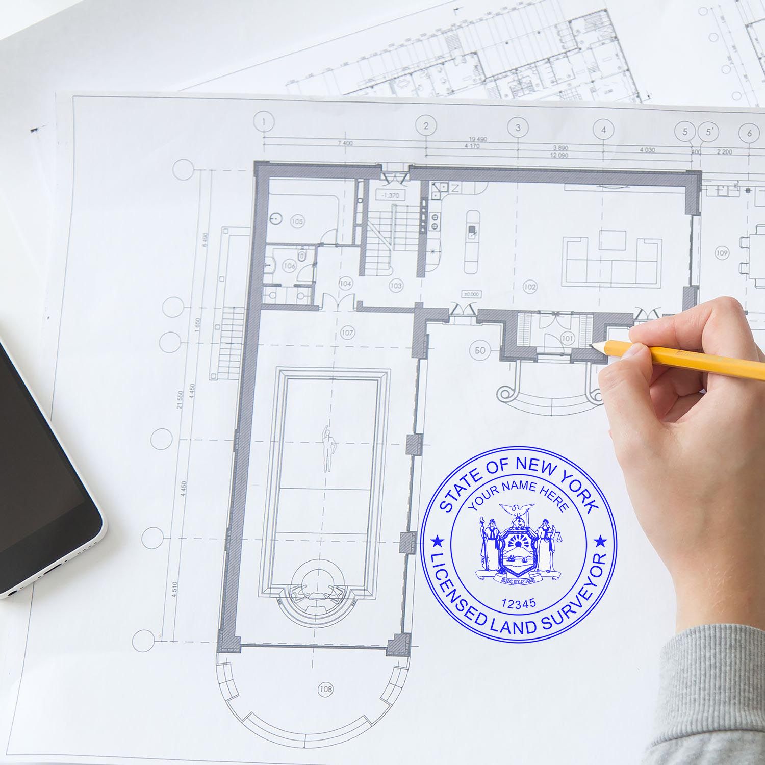 Hand holding pencil over architectural blueprint with Digital New York Land Surveyor Stamp, Electronic Seal for New York Land Surveyor in blue.