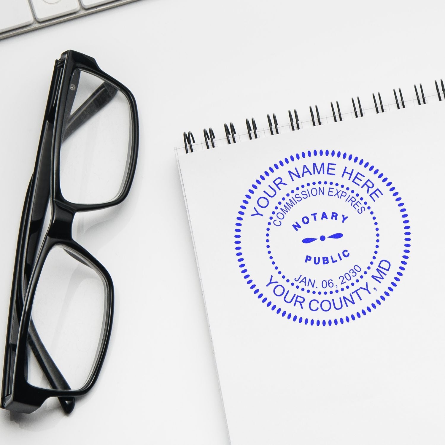 Regular Rubber Stamp of Notary Public Seal on a white notepad, next to black eyeglasses and a keyboard.