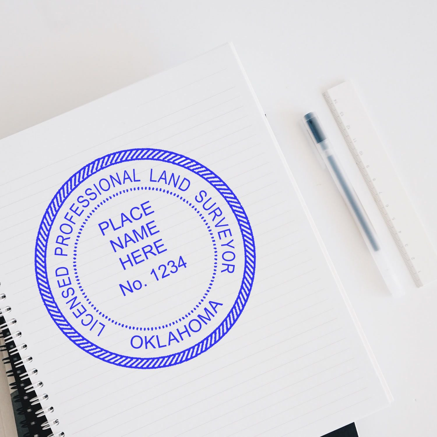 Self Inking Oklahoma Land Surveyor Stamp on a notebook, with a pen and ruler nearby.