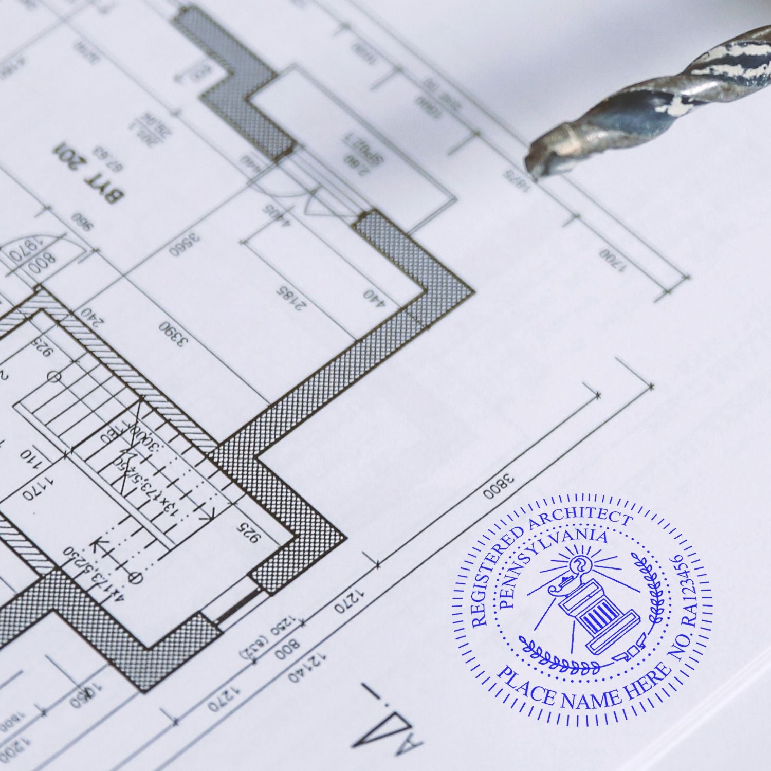 Blueprint with a Premium MaxLight Pre-Inked Pennsylvania Architectural Stamp imprint in blue ink, featuring detailed architectural plans and a drill bit.