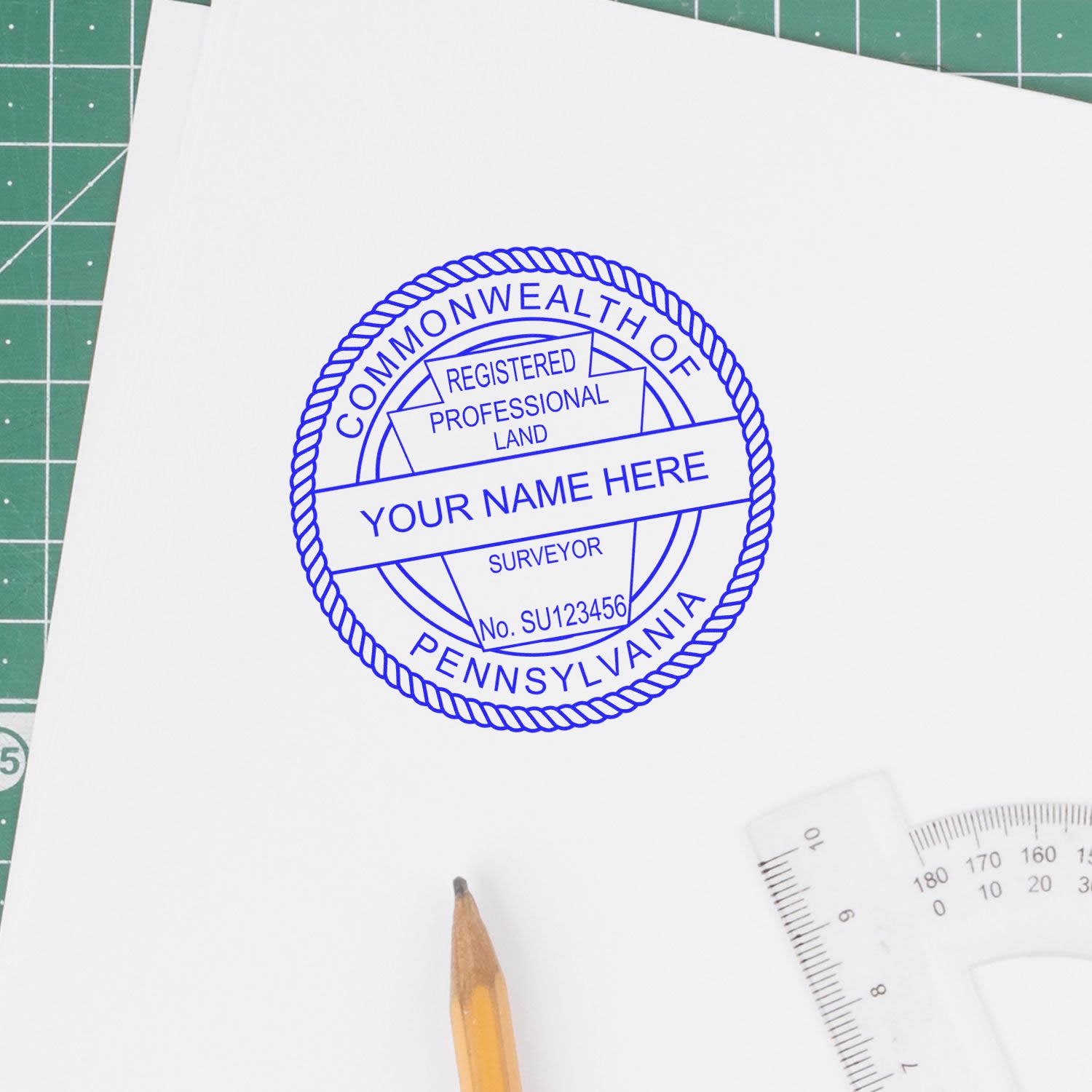 Self Inking Pennsylvania Land Surveyor Stamp in blue ink on white paper, with a pencil and ruler nearby on a green cutting mat.