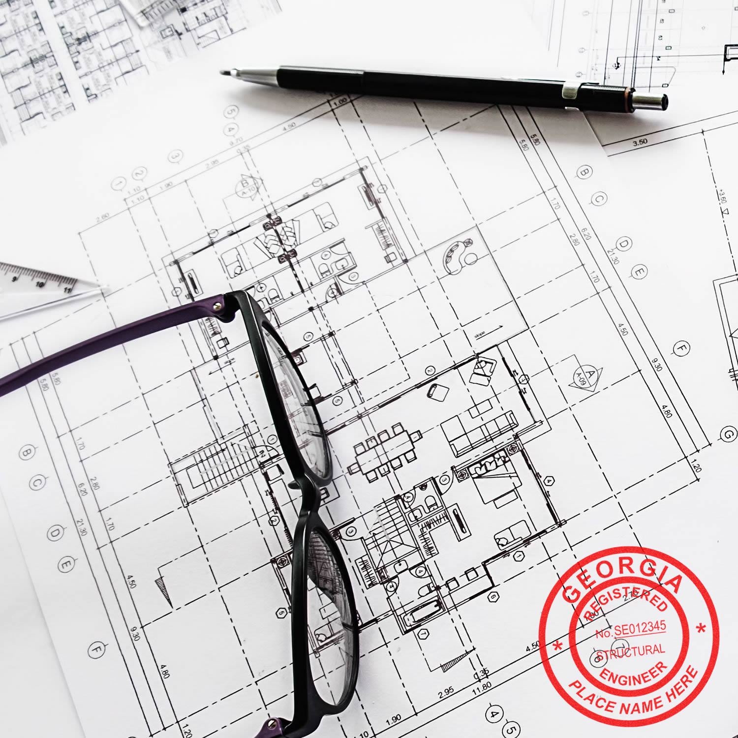 Architectural blueprints with a pair of glasses, a pen, and the Professional Engineer Regular Rubber Stamp of Seal marked Georgia Registered Professional Engineer in red ink.